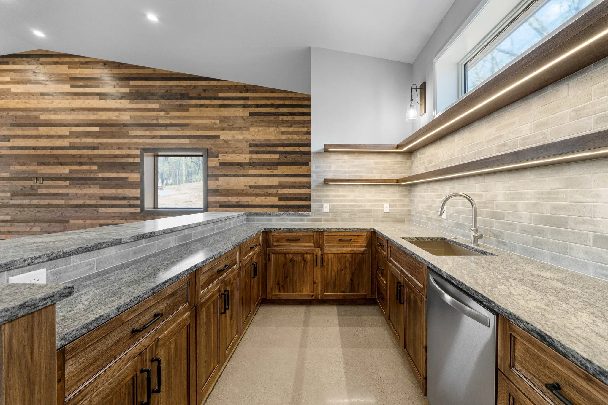 Kitchen with wooden cabinets, granite countertops, brick backsplash, and open shelving, with a window and wood-paneled wall.