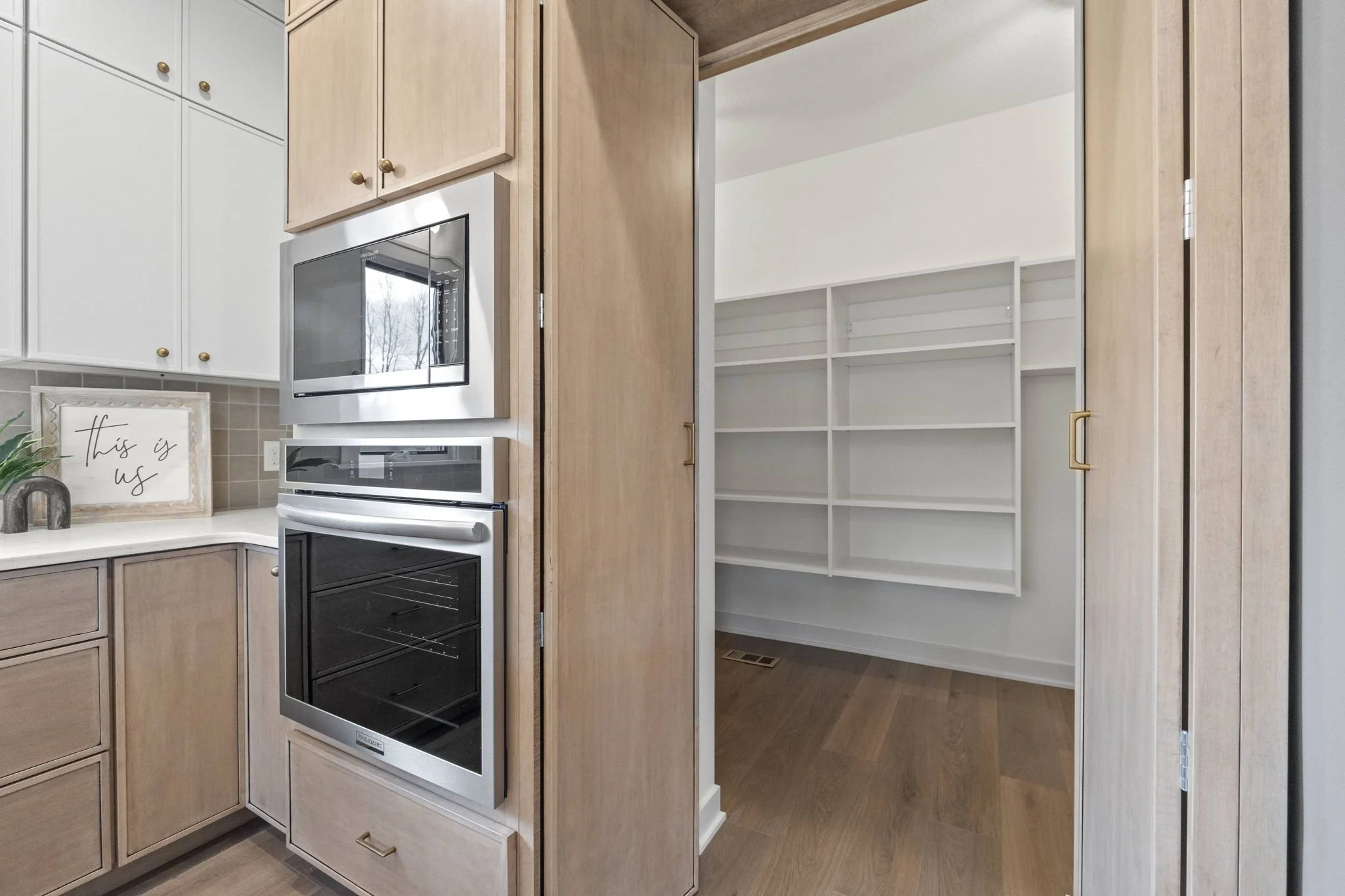 Kitchen with built-in microwave and oven, beige cabinets, a white countertop, and an open pantry with white shelves.