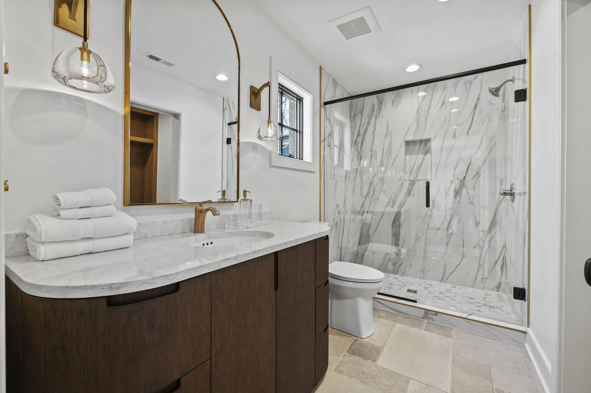 Modern bathroom with marble shower, wooden vanity, and white towels