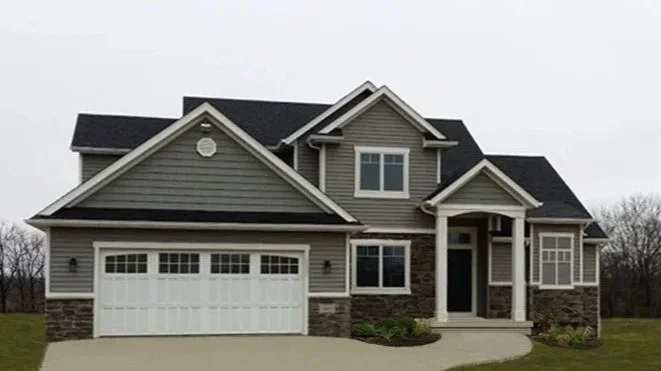 Front view of a large modern house with gray siding, stone accents, and a two-car garage.