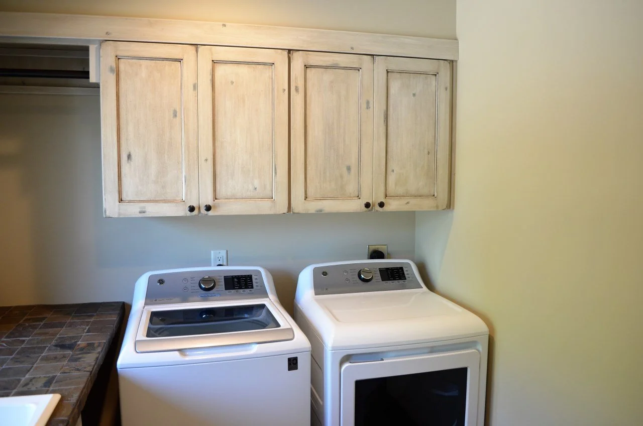 Laundry room with beige wooden cabinets above a washing machine and dryer, with a tiled counter on the left side.