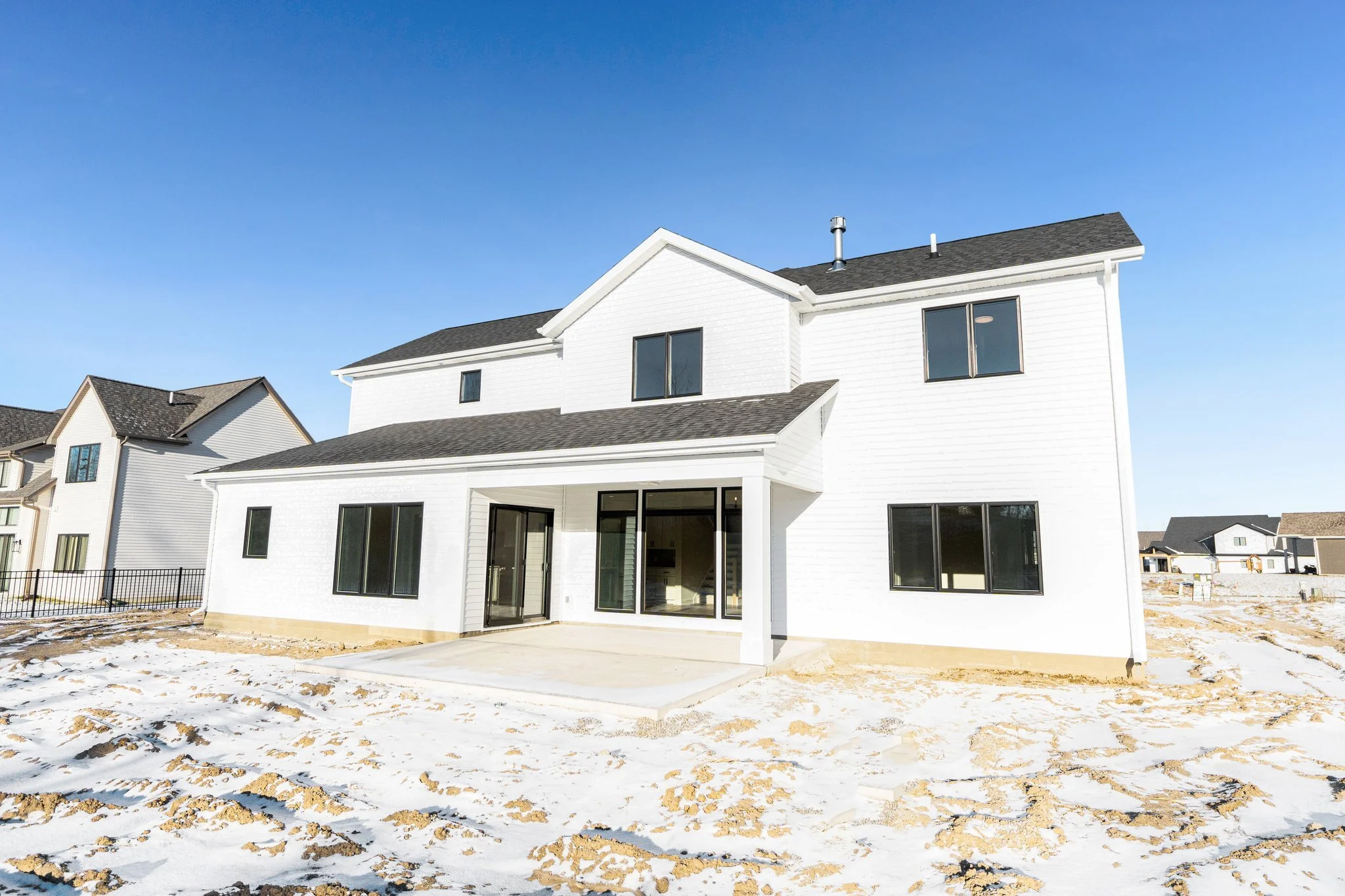 White multi-story house with large windows and a sliding glass door, set on a snow-covered yard with blue sky above.