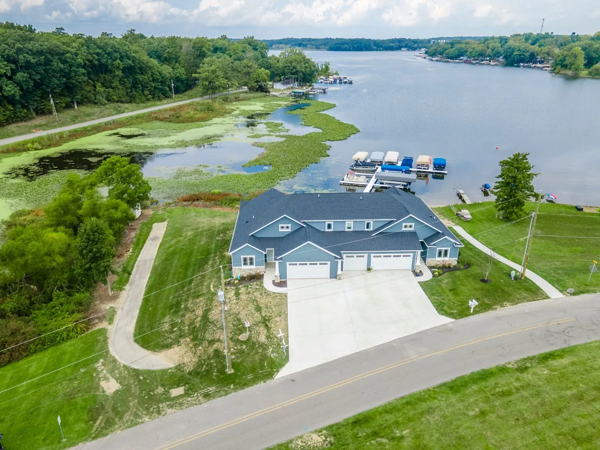 Aerial view of a house by a lake with a boat dock and surrounding greenery.