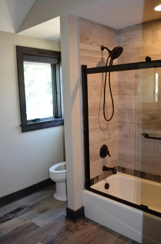 Bathroom with a bathtub and a glass shower enclosure, black fixtures, and a window with black trim.