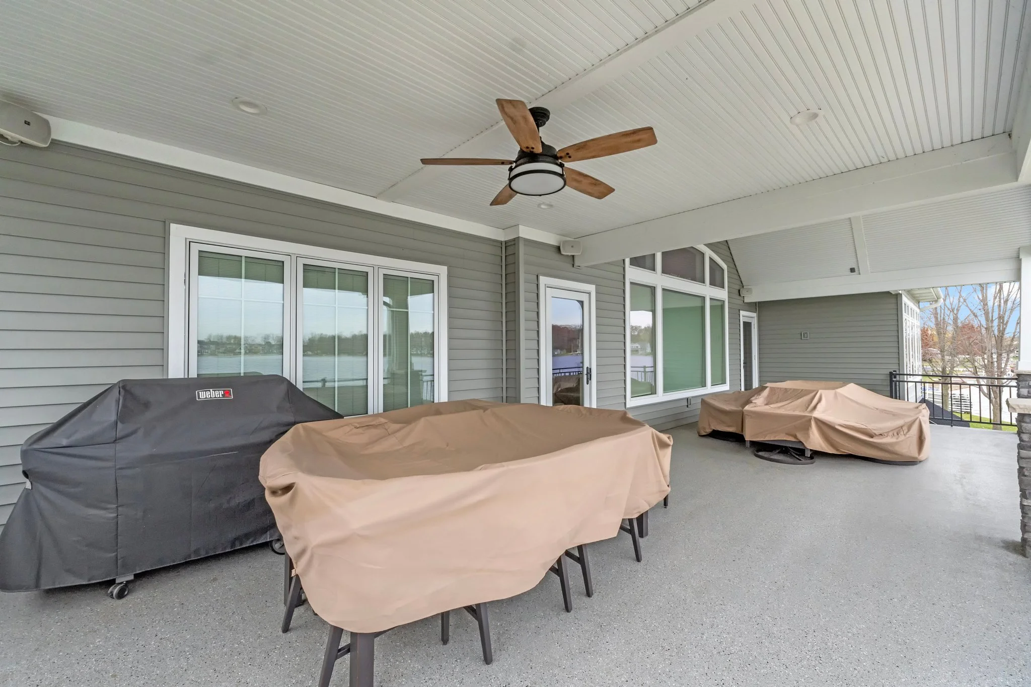 Covered outdoor furniture on a spacious screened porch with a ceiling fan and large windows.