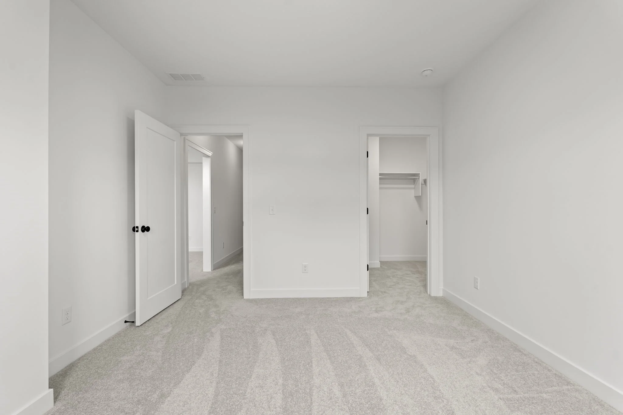 Empty bedroom with white walls, beige carpet, and two open closet doors.