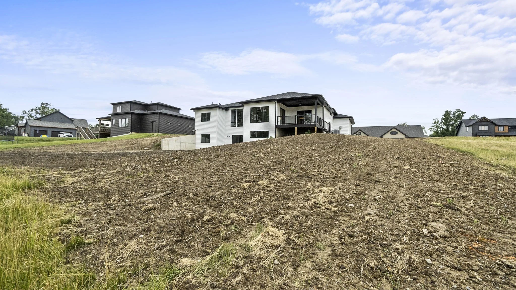 Residential area on a hill with new houses, partly bare soil, and a cloudy sky.