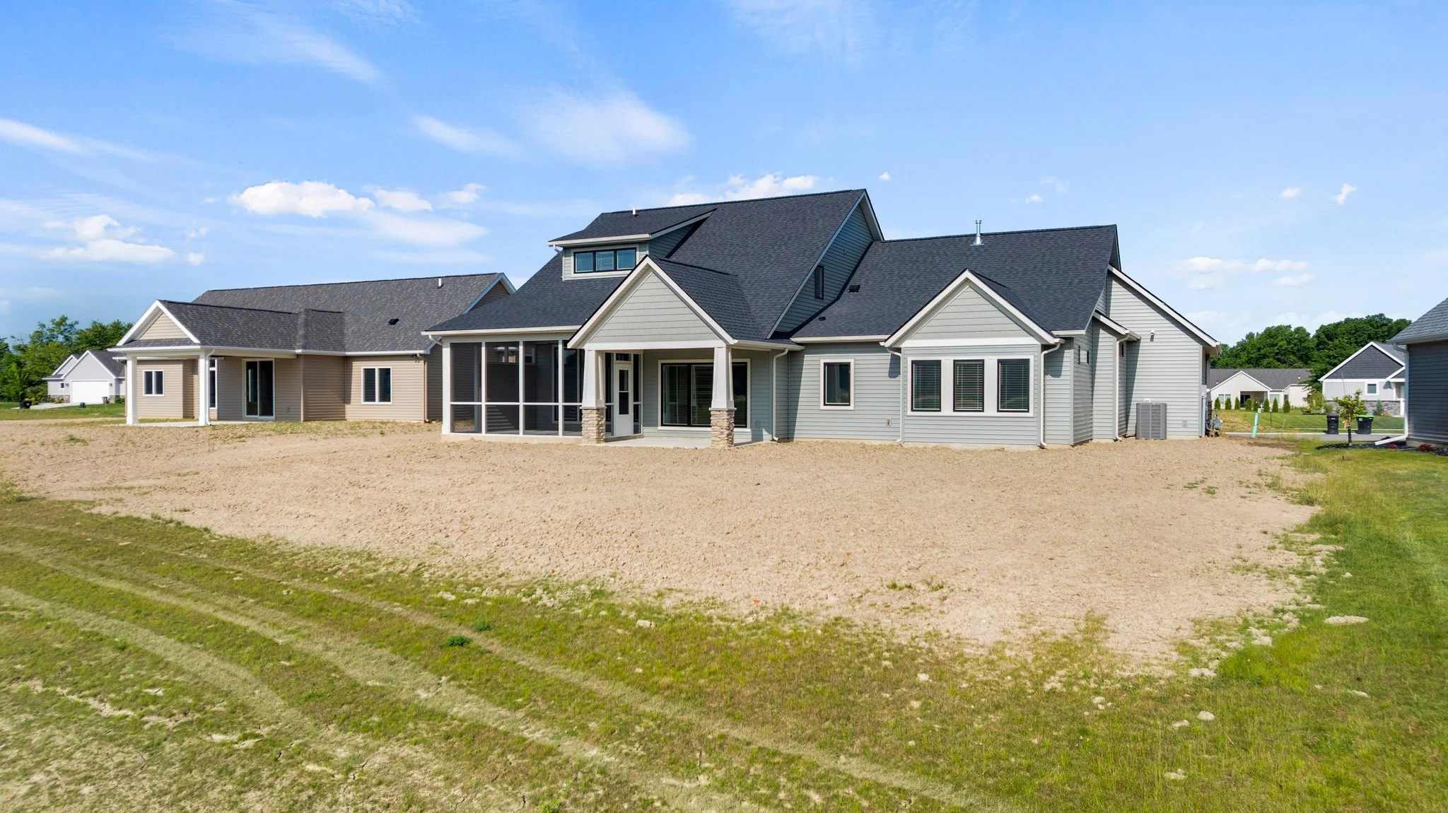 Newly built backyard house with gray siding, black roof, and a screened porch, under a blue sky with clouds.