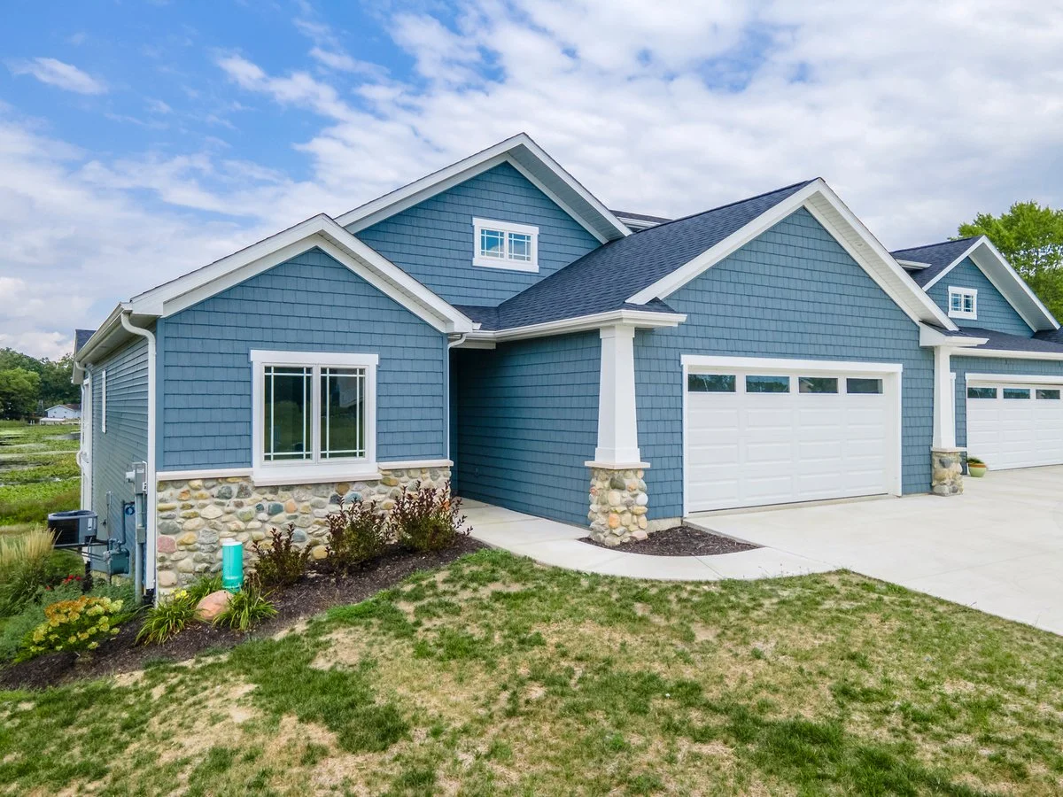 Blue house with stone accents, white garage doors, and well-maintained lawn.