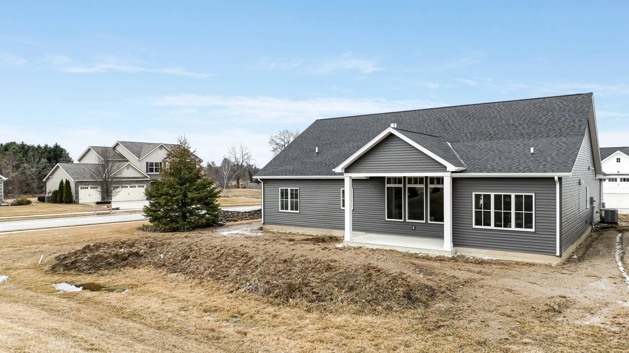 New gray house under construction in a suburban neighborhood with other finished homes, a lawn, and a blue sky.