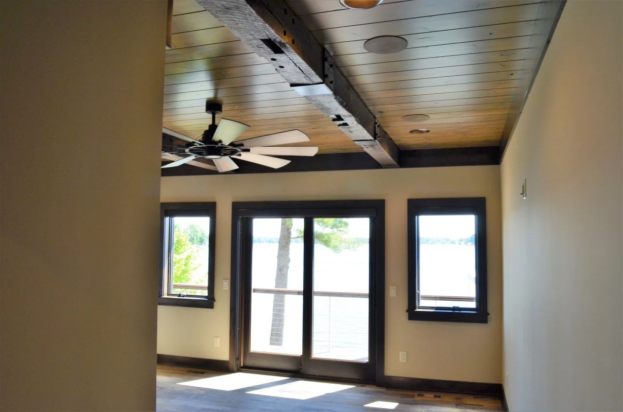 Interior of a room with a wooden ceiling, a ceiling fan, three windows, and a glass door leading outside.