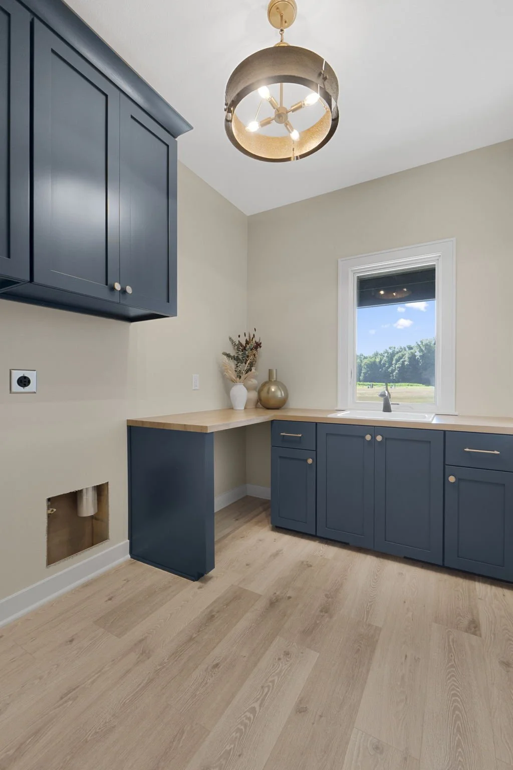 A modern kitchen with blue cabinets, a light wood countertop, a window showing an outdoor landscape, and a ceiling light fixture.