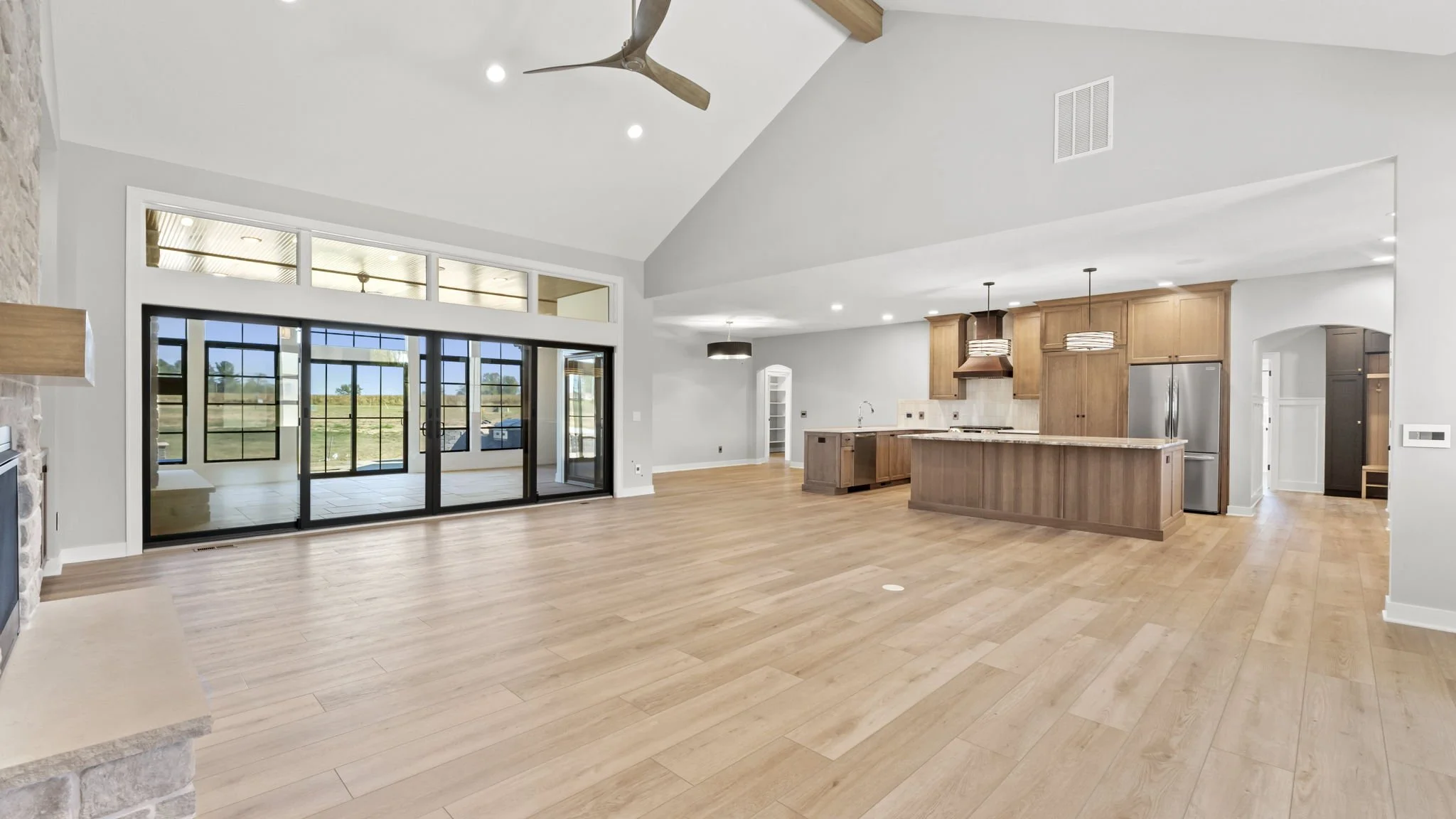 Open concept living space with hardwood floors, a kitchen with wooden cabinets, stainless steel appliances, and a large island. A ceiling fan and pendant lights hang from the ceiling, and there are sliding glass doors leading to an outdoor area with 