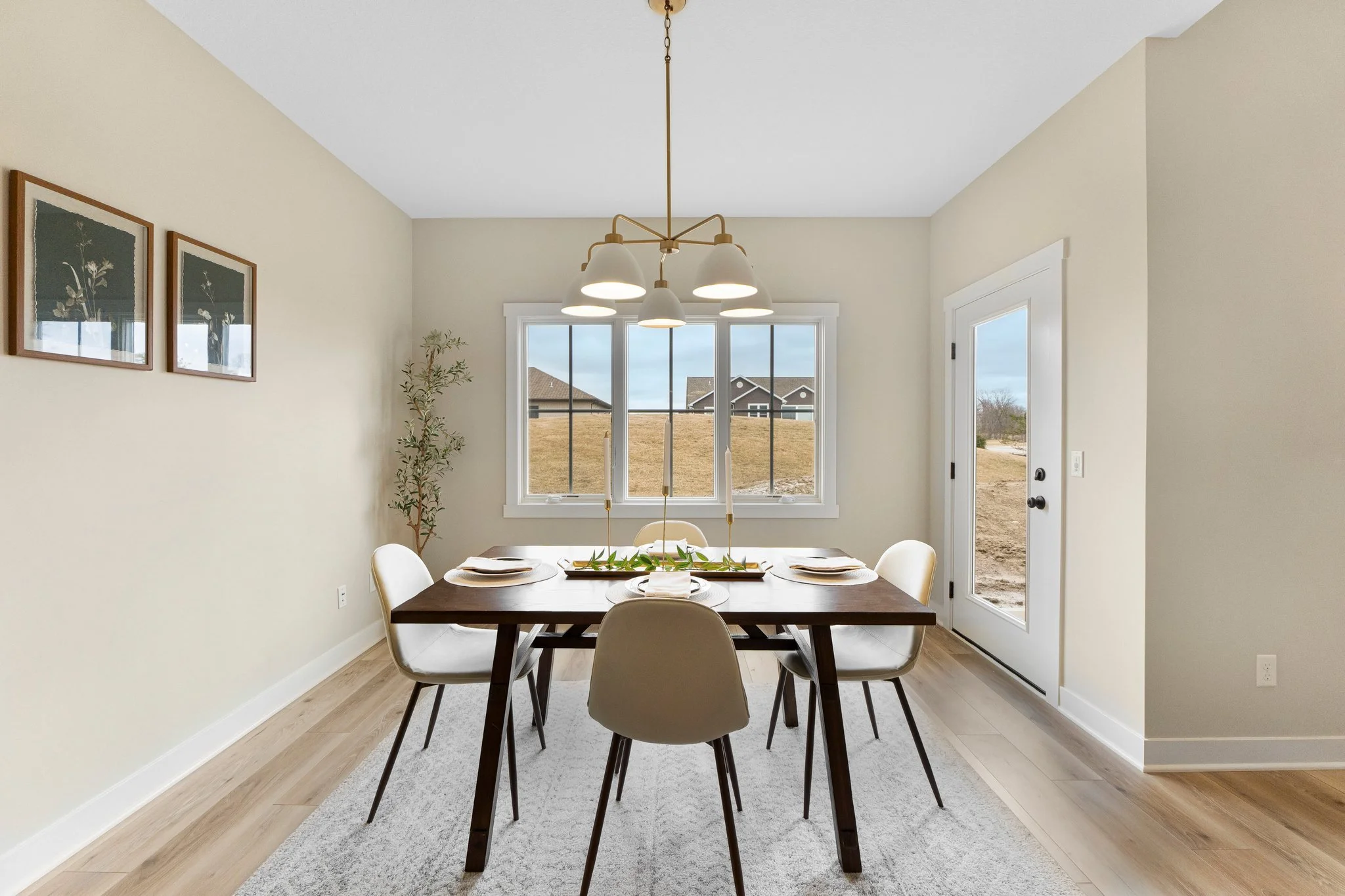 Dining room with a wooden table and six white chairs, a large window, a door, a chandelier, and a potted plant.