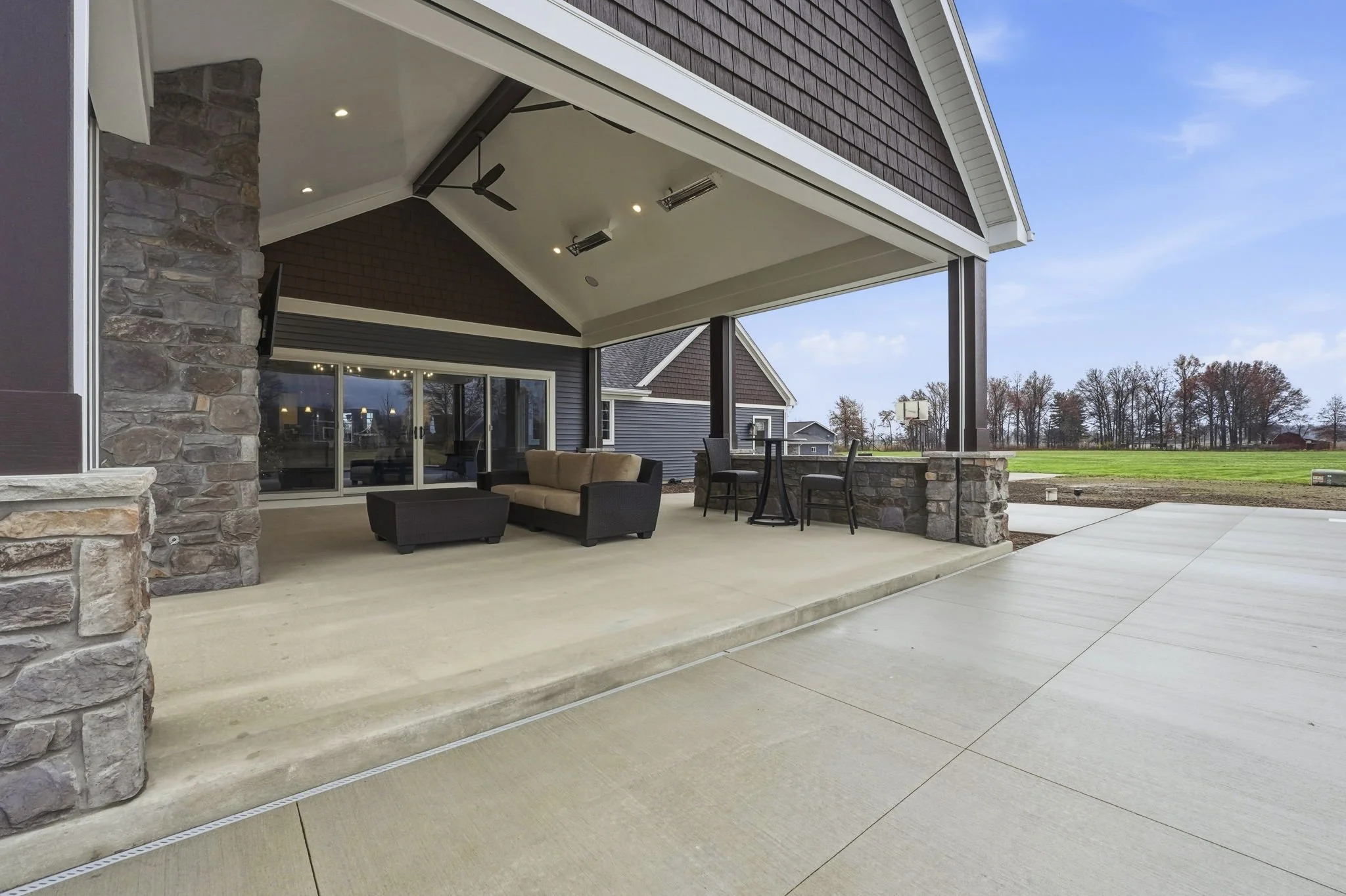 Covered outdoor patio with lounge furniture and bar-height table, overlooking a field and trees in the distance.