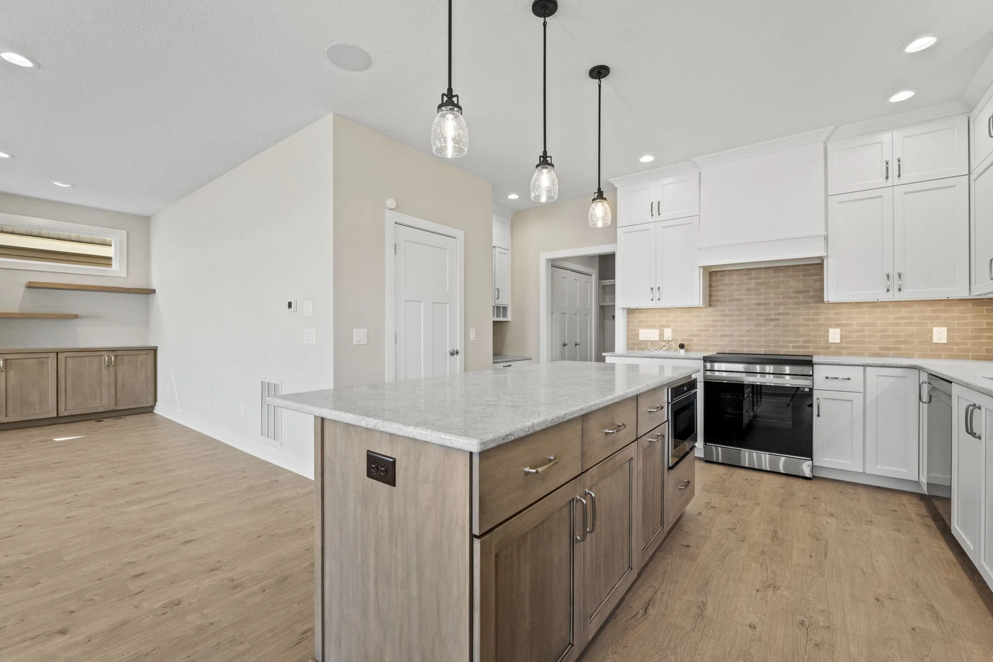 Modern kitchen with white cabinets, a large island with a light wood base, and a stainless steel oven. Overhead pendant lights and wood flooring.