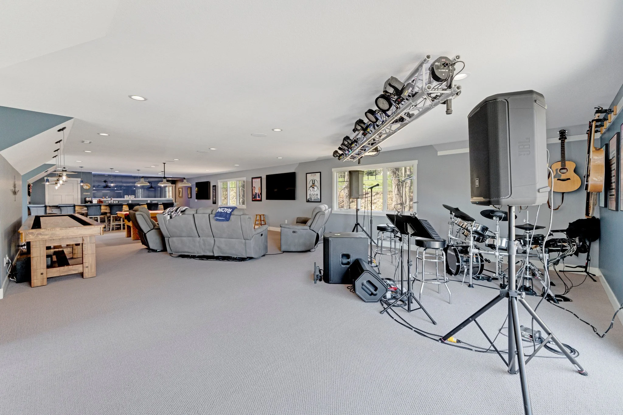 A spacious basement with a musical setup including drums, guitars on the wall, microphones, and speakers. There is a seating area with couches and a TV.