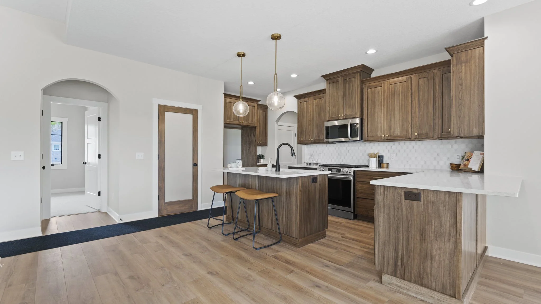 Modern kitchen with wood cabinetry, white countertops, stainless steel appliances, and pendant lights over the island, with hardwood floors and white walls.