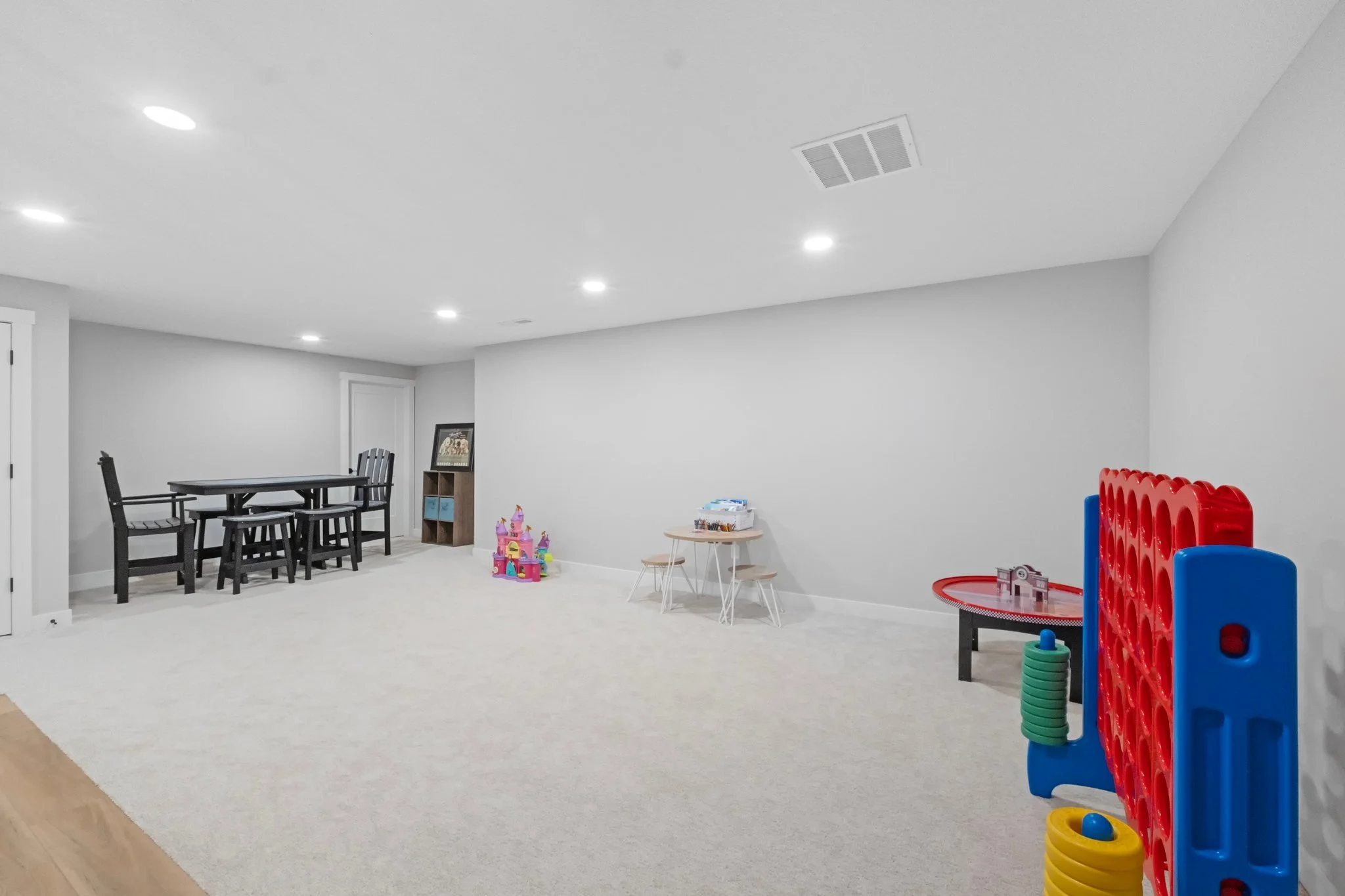 Spacious basement playroom with children's toys, table, chairs, and game setup, illuminated by ceiling lights.