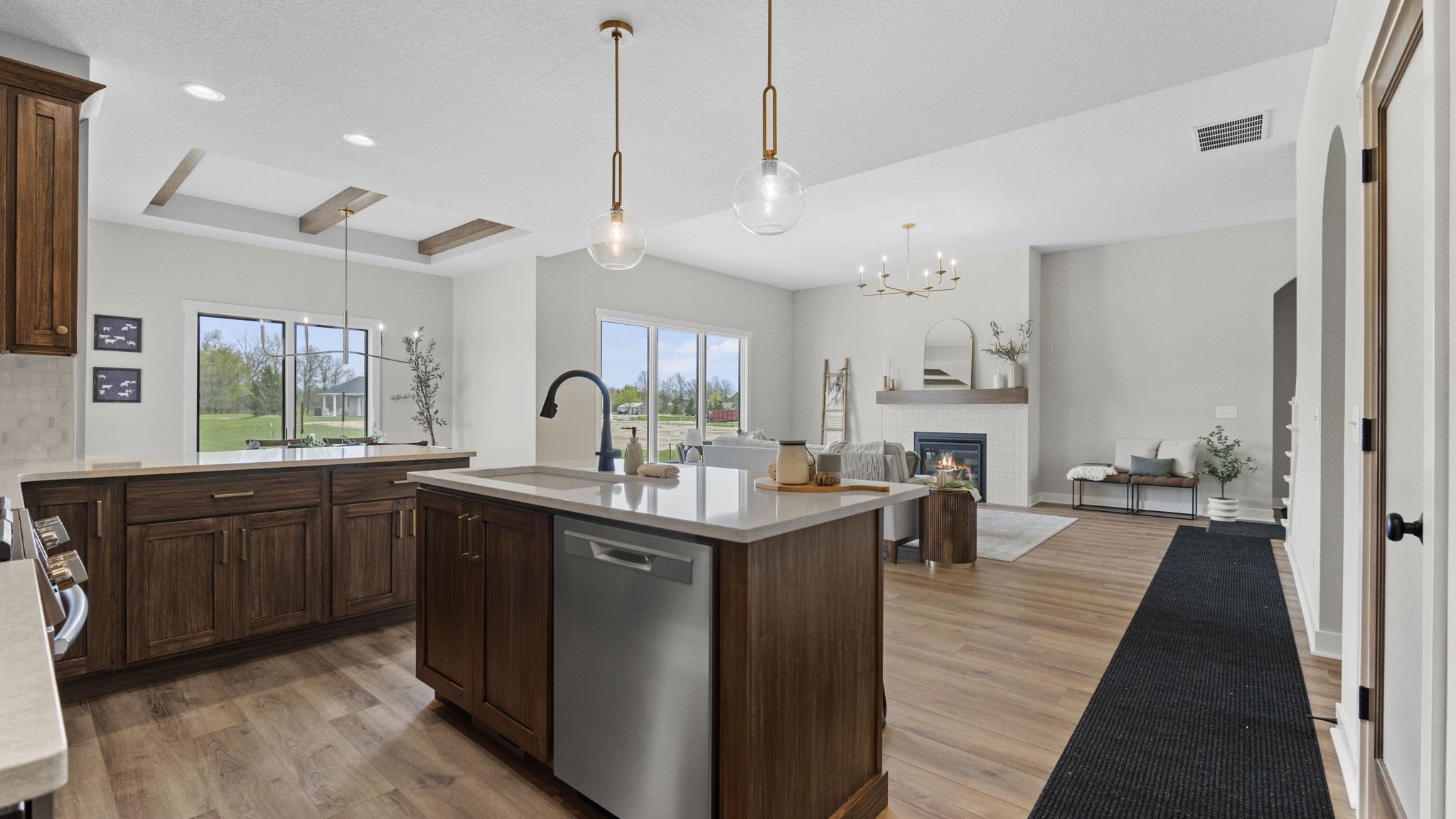 Open-concept kitchen and living room with wooden cabinets, white countertops, pendant lighting, large windows, fireplace, and hardwood floors.
