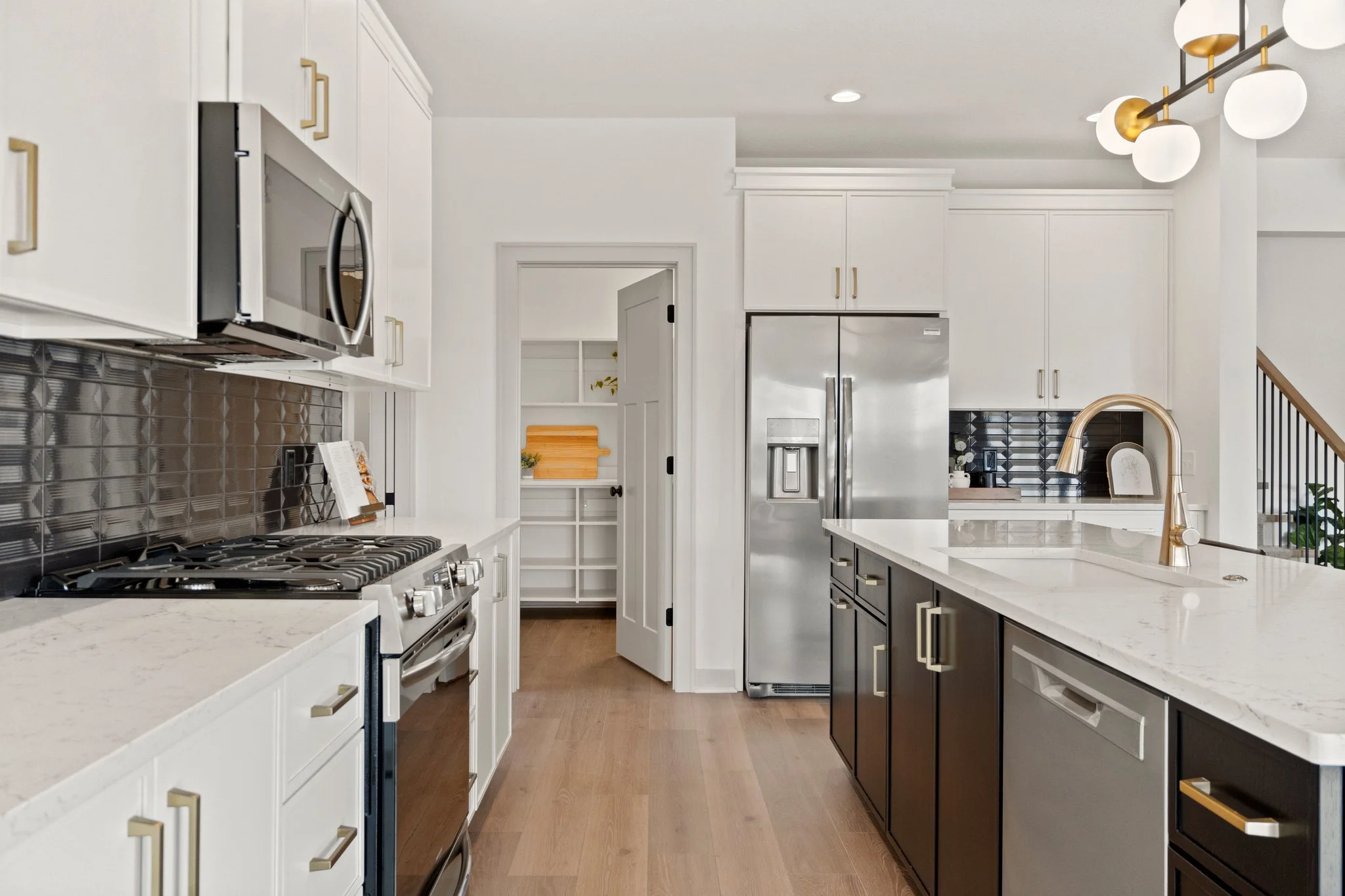 Modern kitchen with white and black cabinets, marble countertops, stainless steel appliances, a black backsplash, and a gold faucet, with hardwood flooring.