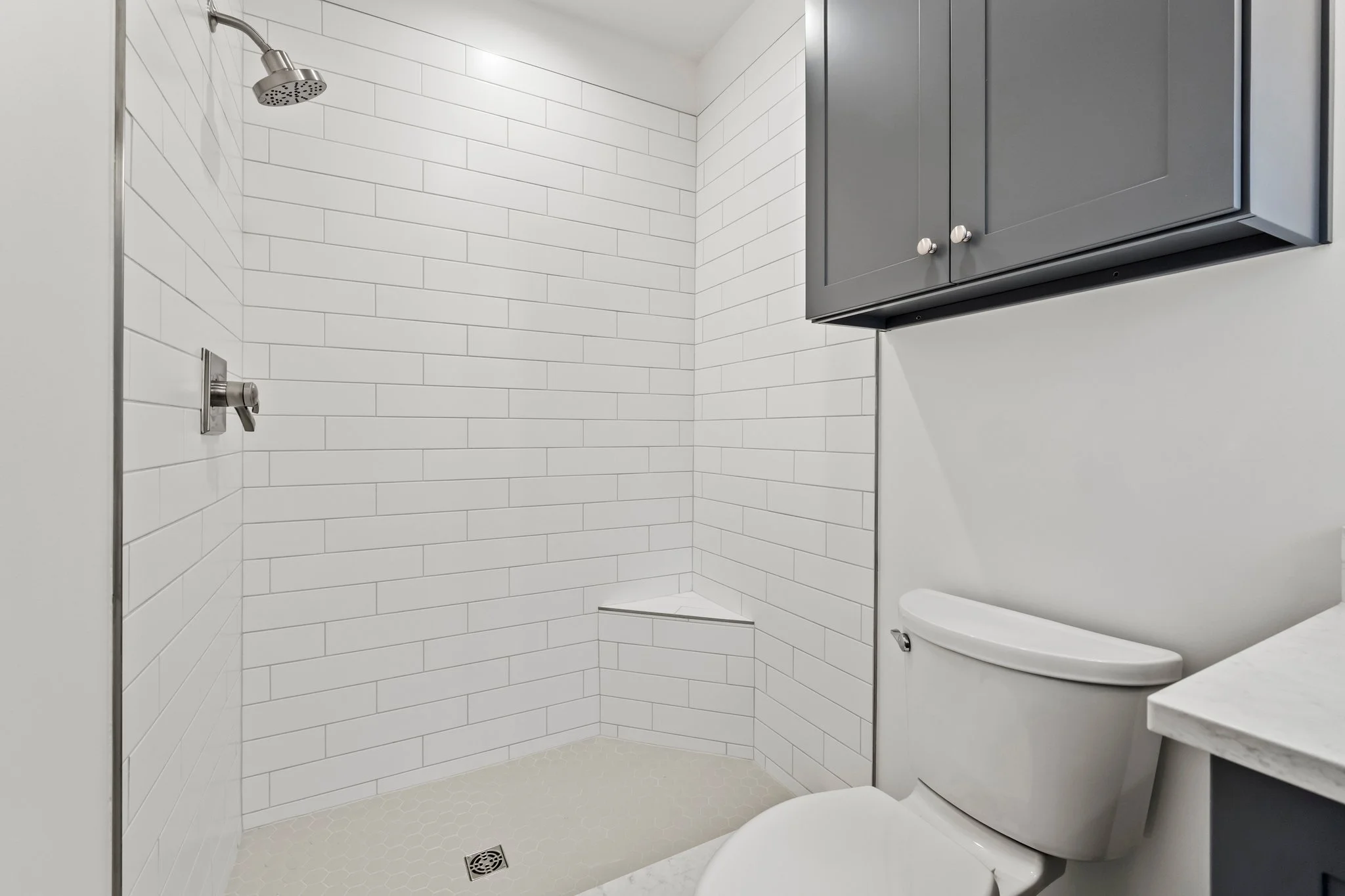 A modern bathroom with a white tiled shower, gray cabinet, and a white toilet.