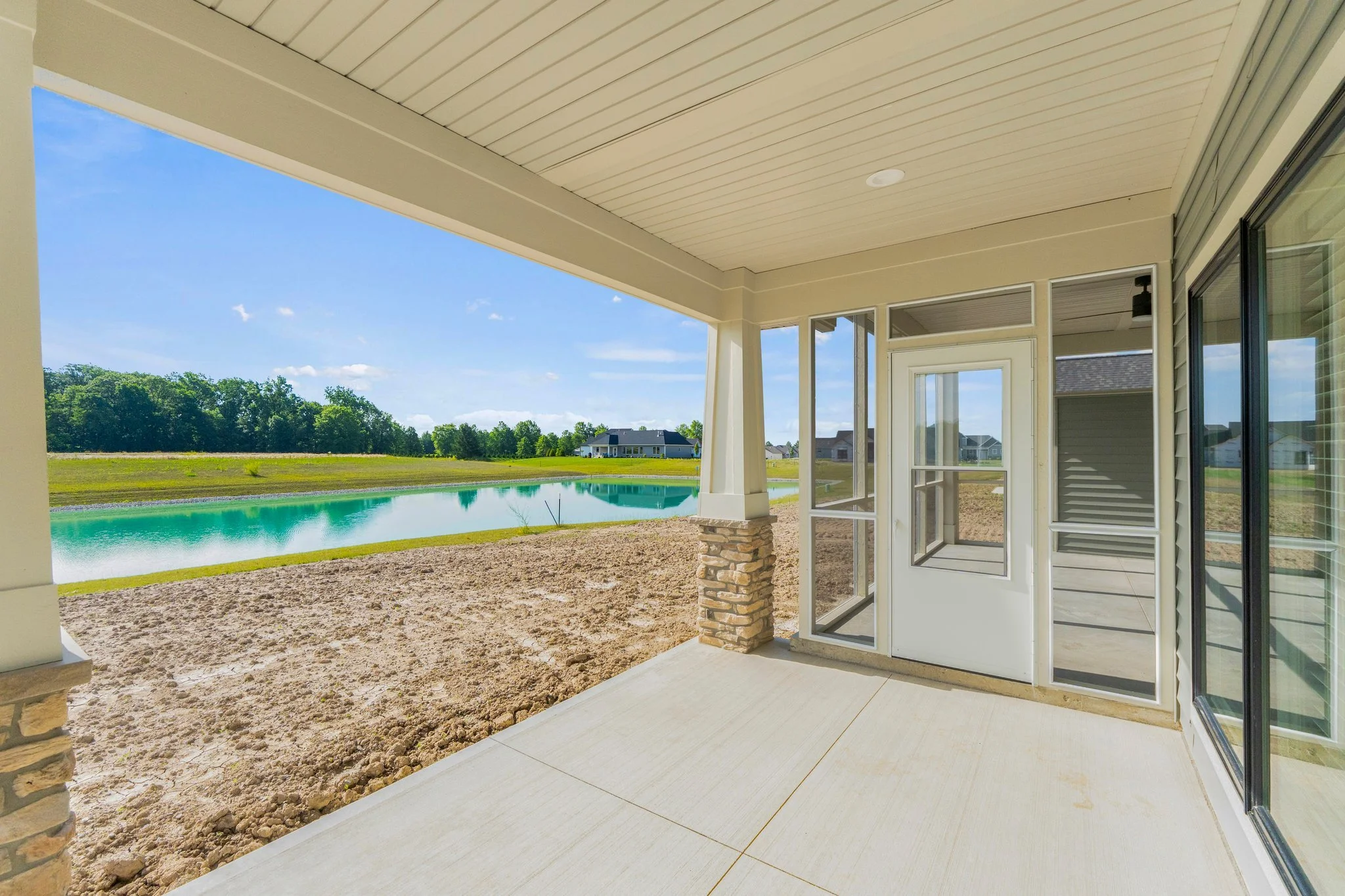 View from a covered patio overlooking a large pond with houses in the distance, under a partly cloudy blue sky.