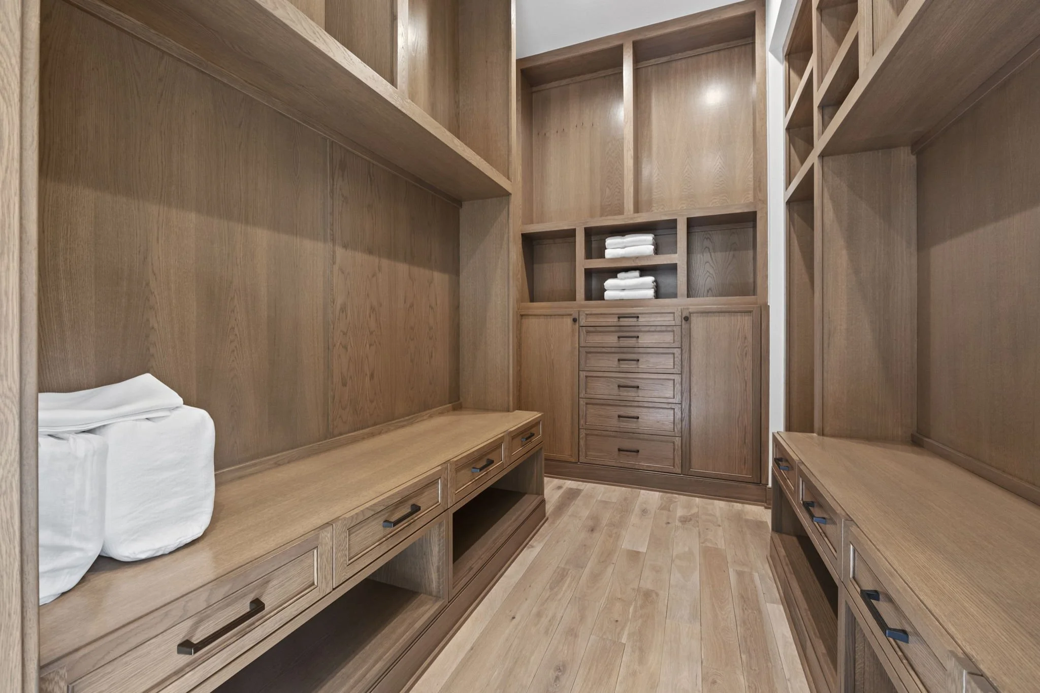 Empty walk-in closet with wooden shelves, drawers, and benches, with folded towels on shelves.