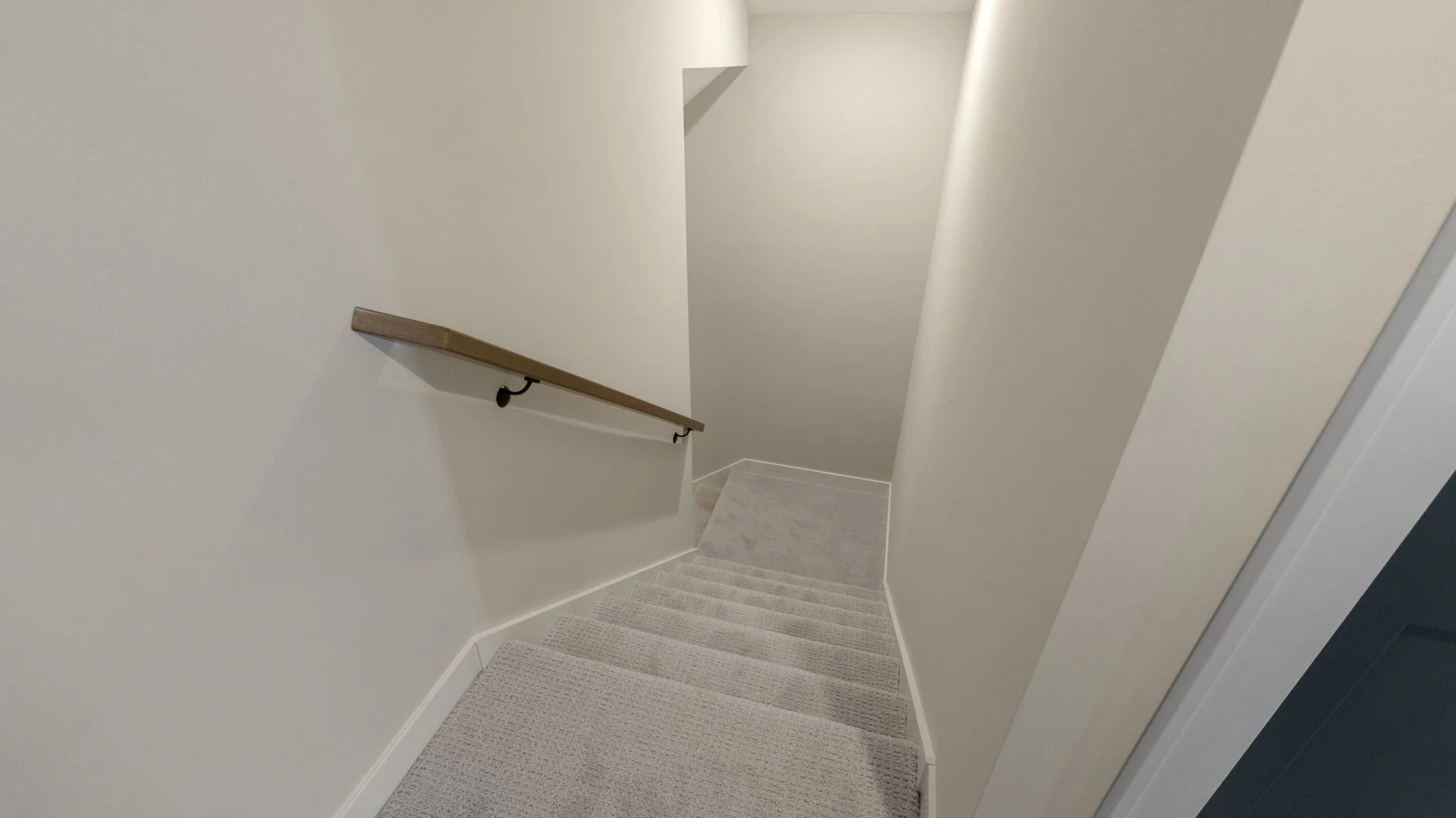 Indoor staircase with beige carpet, white walls, and a wooden handrail on the left side.