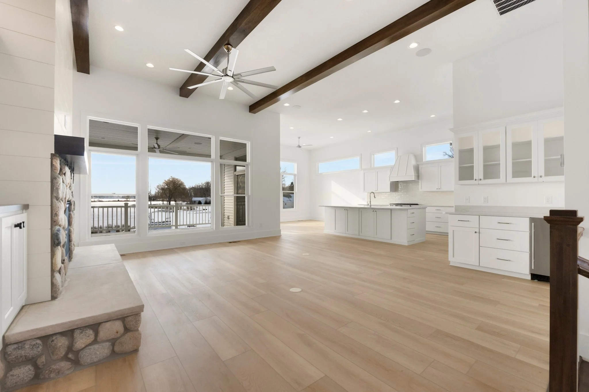 Spacious open-concept living area and kitchen with white cabinets, light wood flooring, and large windows bringing in natural light.
