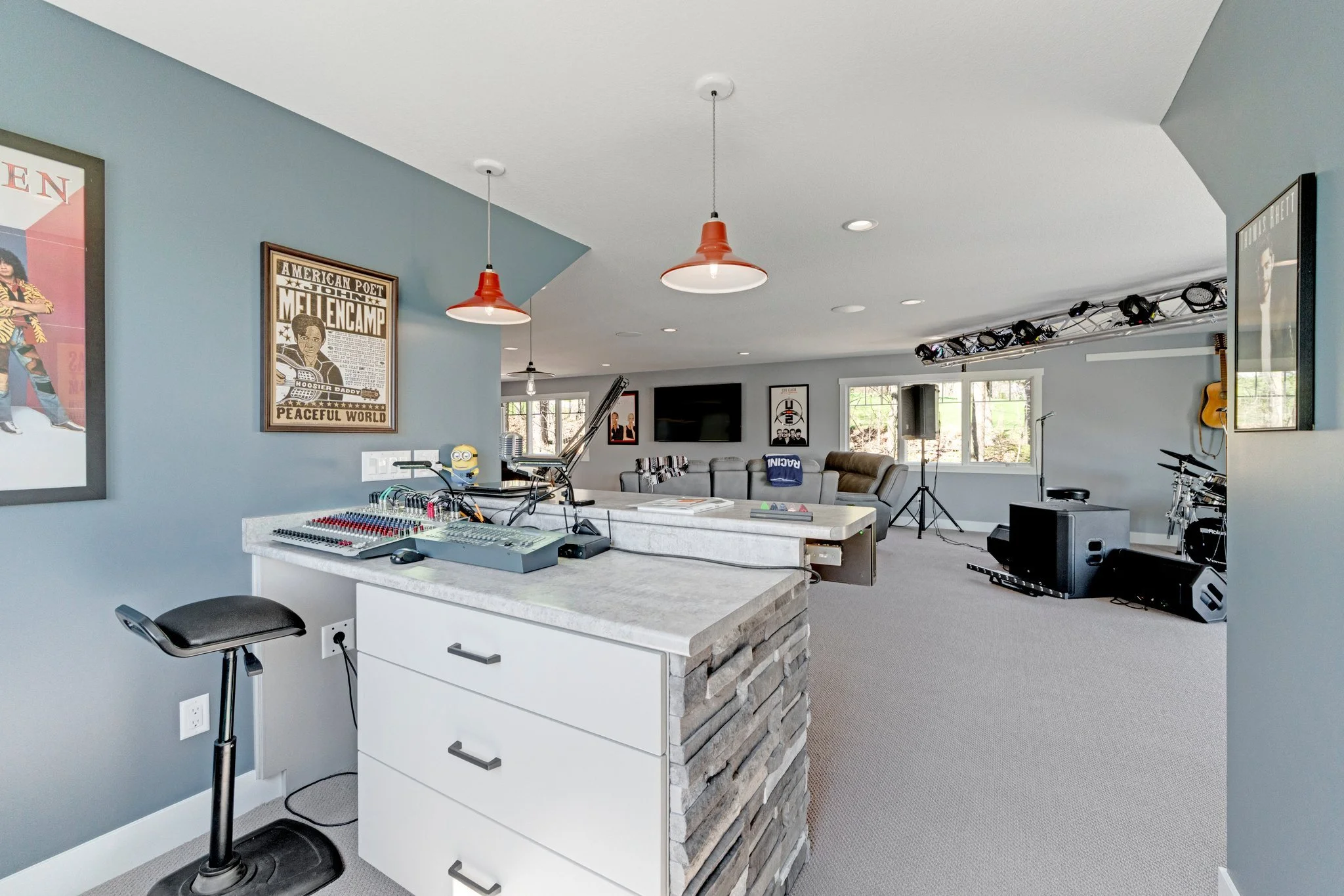 A spacious basement entertainment room with a seating area, musical and DJ equipment, and large windows letting in natural light.