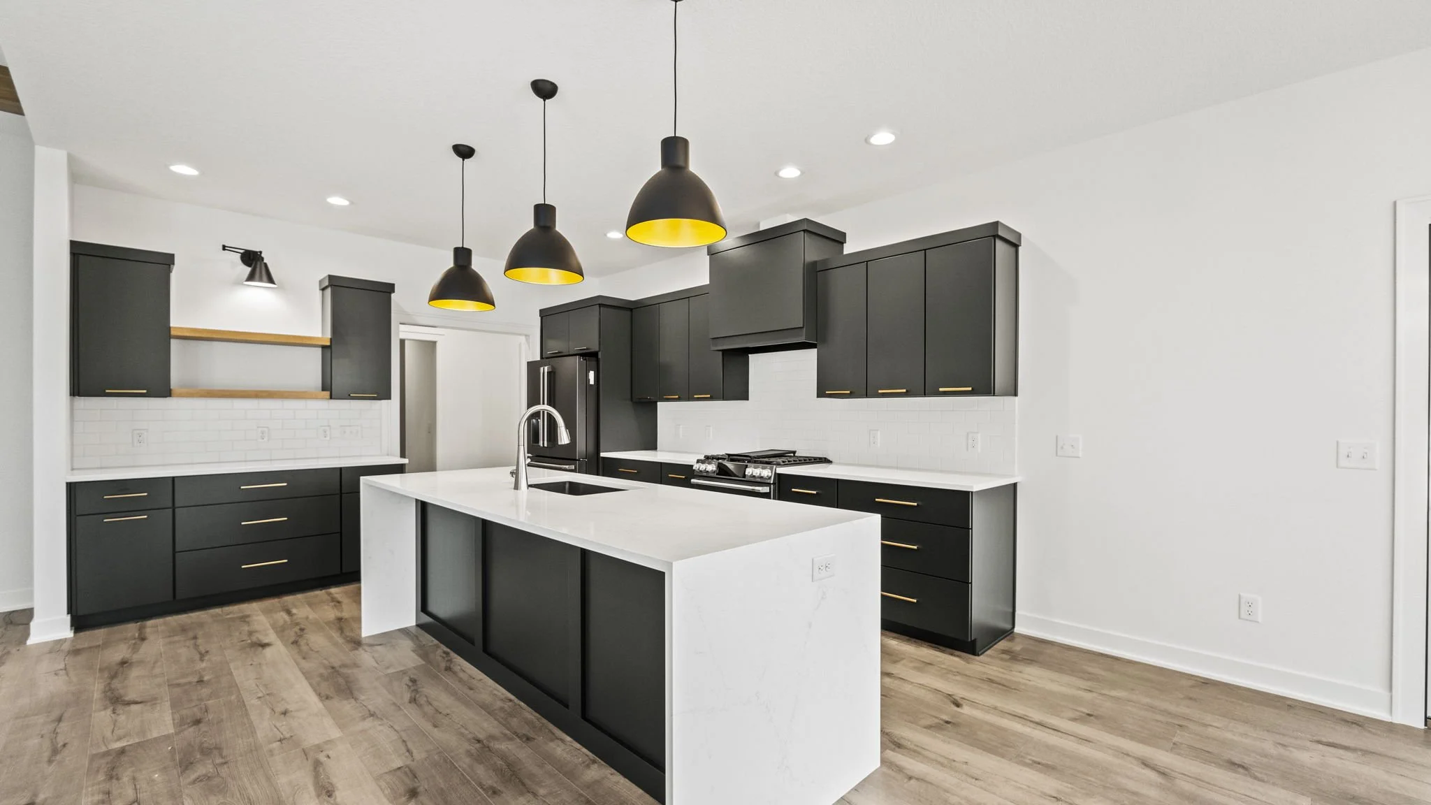 Modern kitchen with black cabinets, white countertops, a central island with a sink, and pendant lighting with yellow interior details.