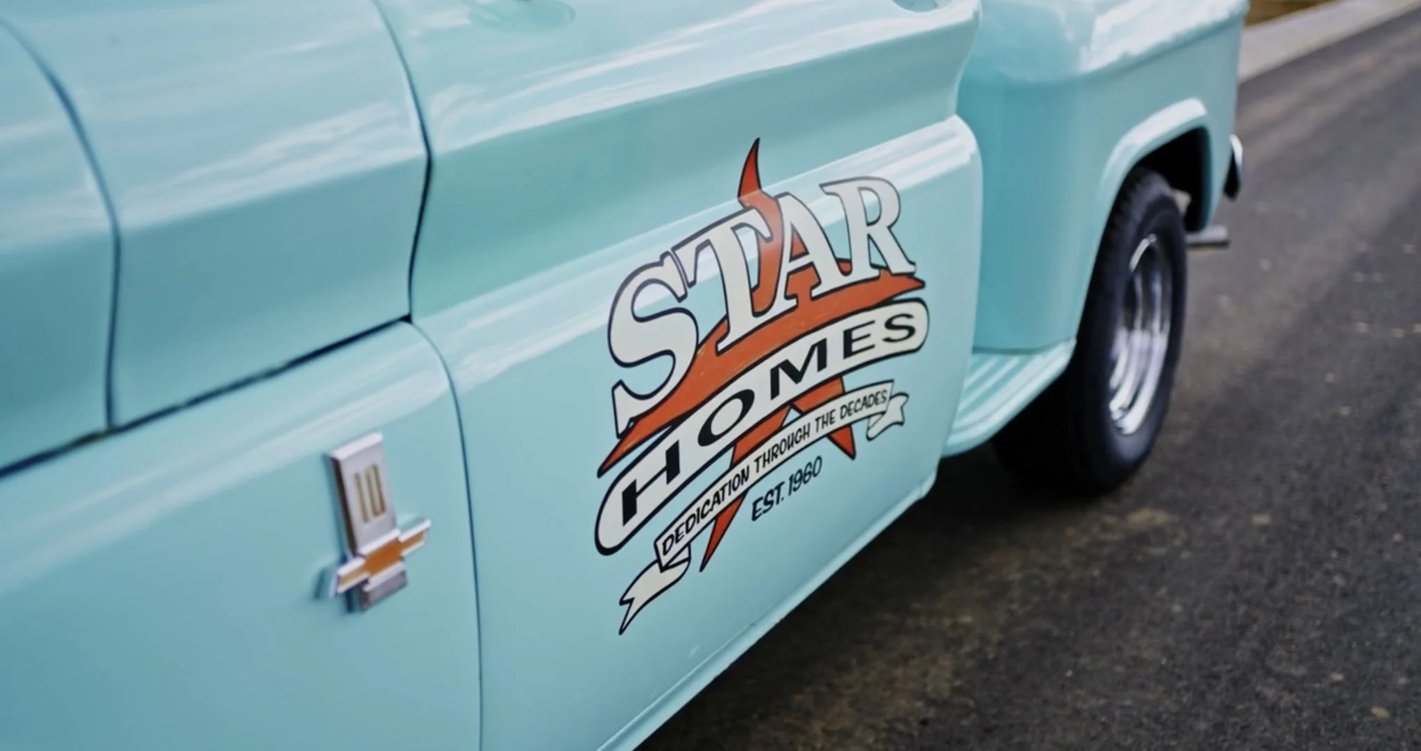 Close-up of a vintage light blue Chevrolet vehicle with a decal that reads 'Star Homes'. The decal includes a slogan 'Dedication Through the Decades' and 'Est. 1960'.