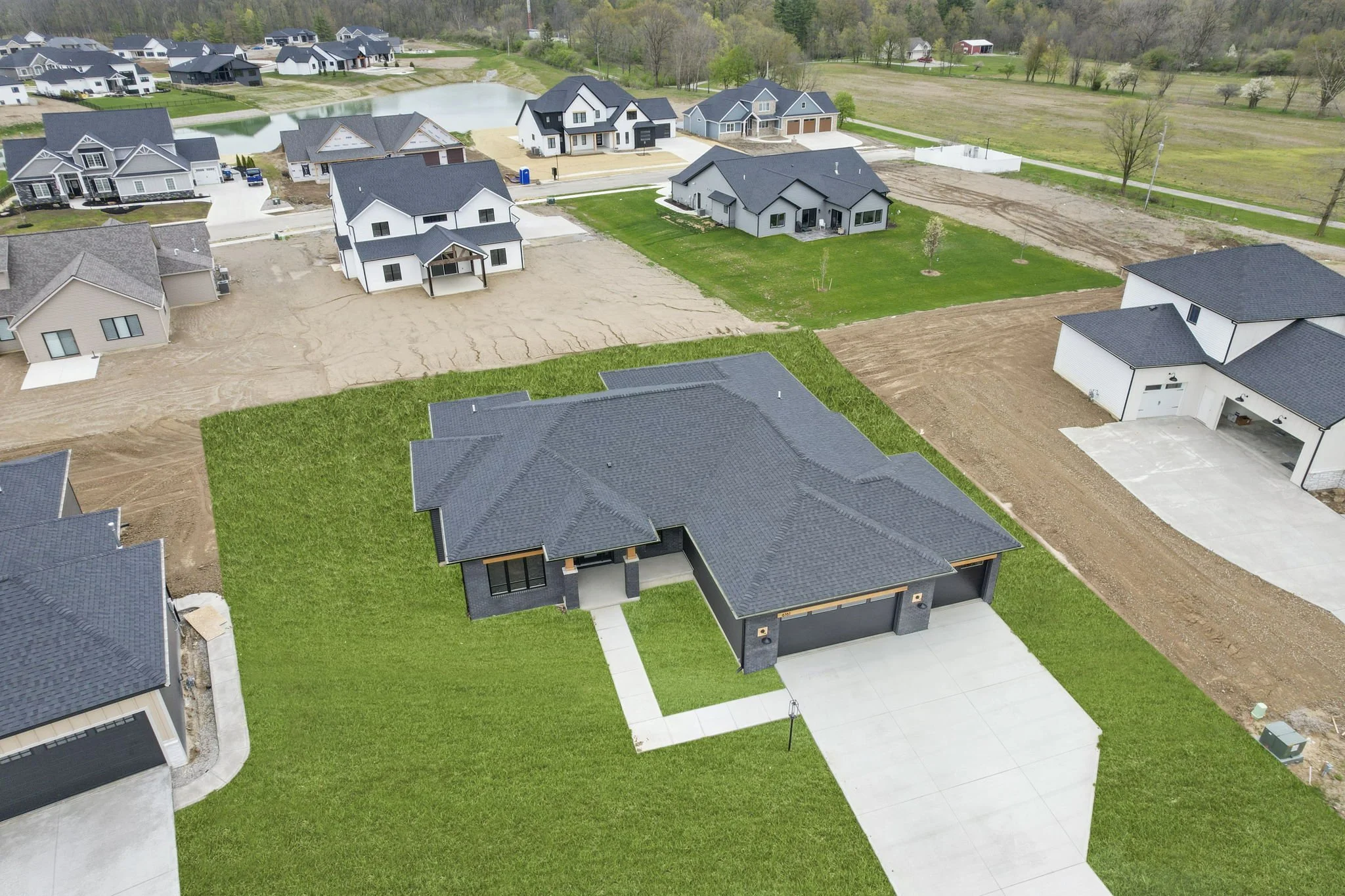 A newly built modern house with a black roof, green lawn, and driveway in a neighborhood under construction.