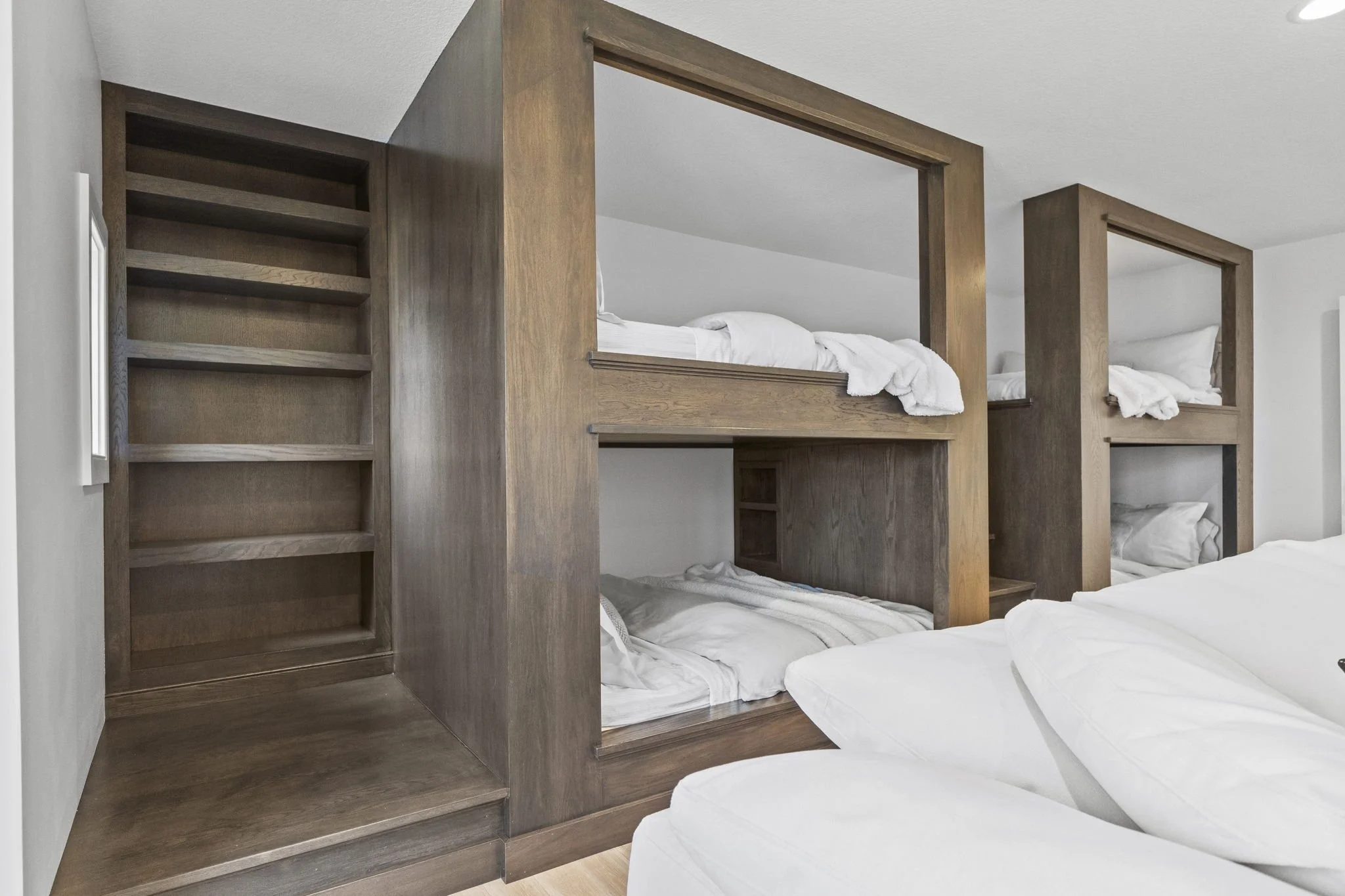Wooden bunk beds in a hotel room, with a staircase on the left, and two sets of beds on top and bottom stacked vertically, with white linens and pillows.