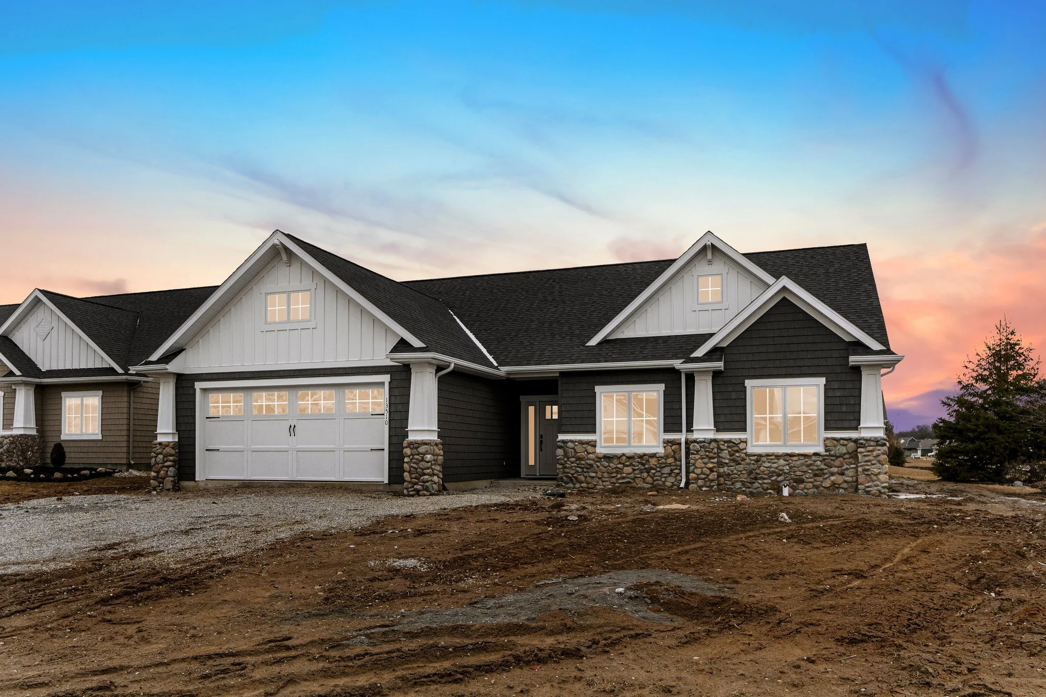 Newly built house with a dark exterior, white trim, stone accents, and a garage, set against a colorful sunset sky.