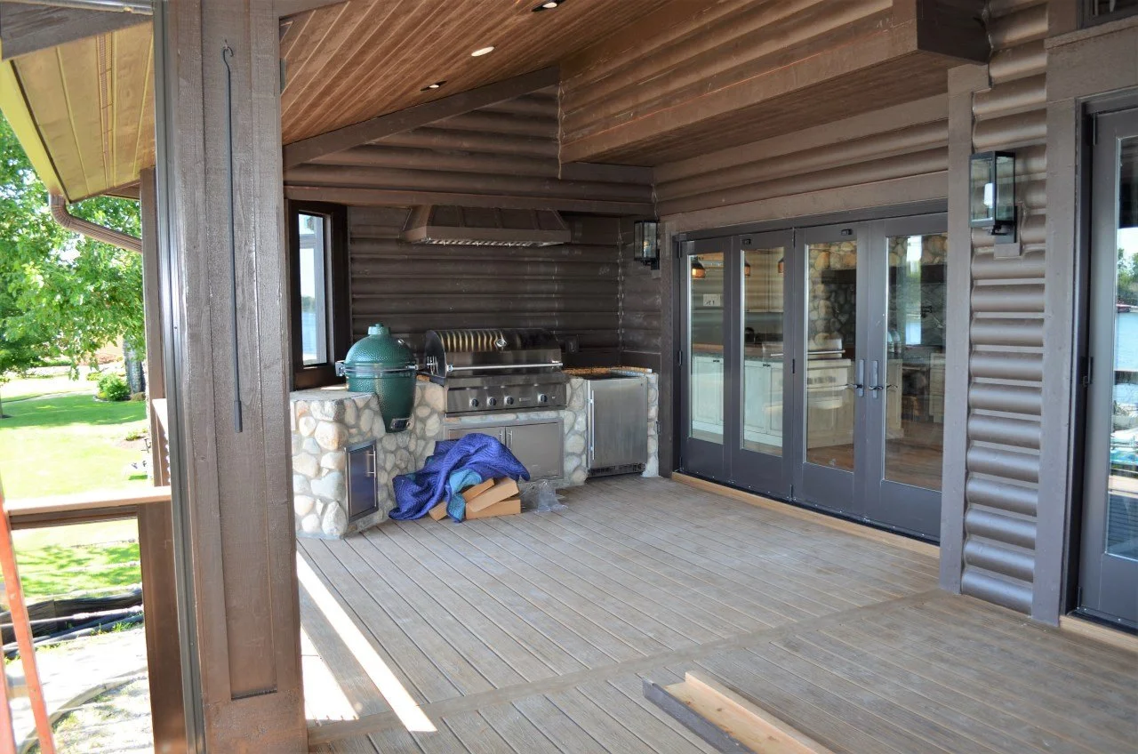 An outdoor patio with a built-in grill, stone counter, and sliding glass doors leading inside a house.