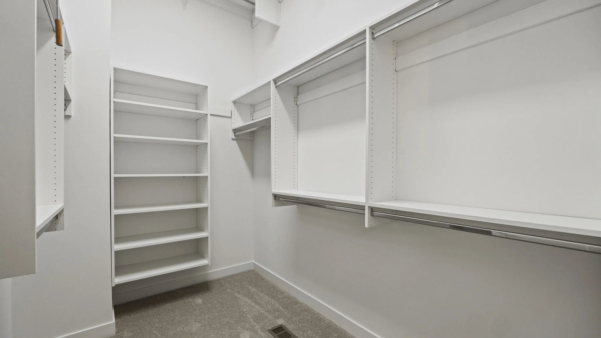 Empty white walk-in closet with shelves, hanging rods, and beige carpet.