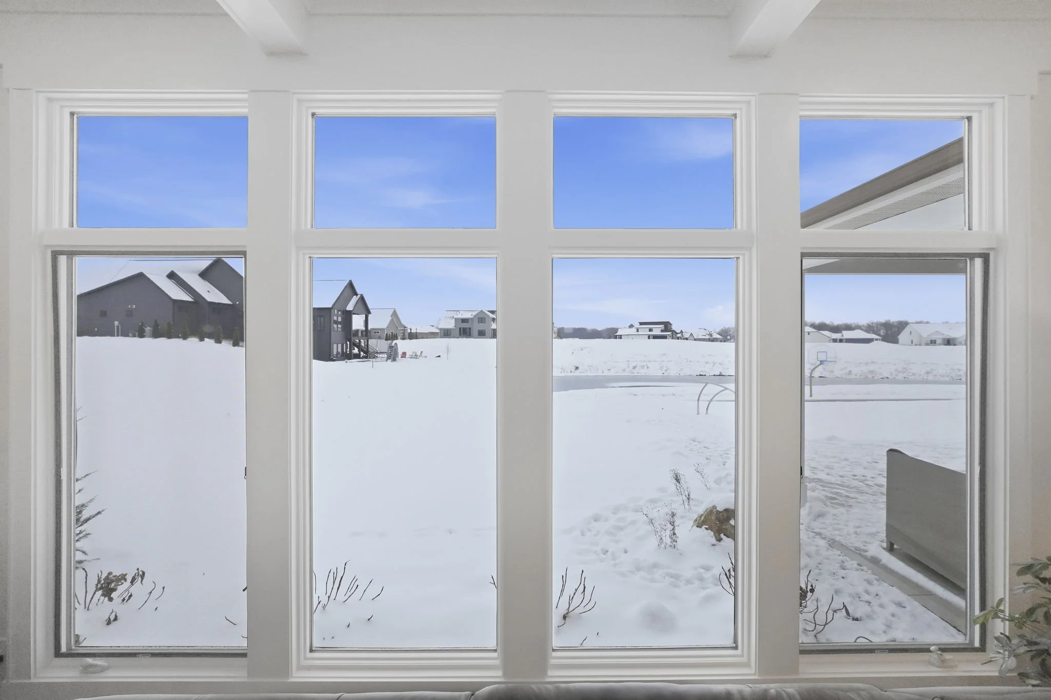 View of snowy landscape with houses and blue sky through large window