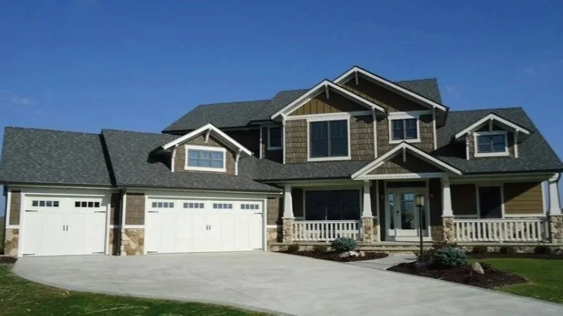 Large two-story house with three garages, a front porch, and a well-maintained lawn, under a clear blue sky.