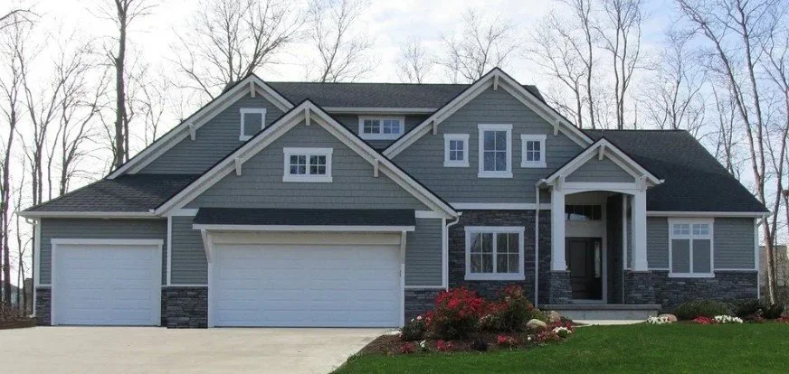 A large grey two-story house with a three-car garage, front steps, and a landscaped lawn with bushes