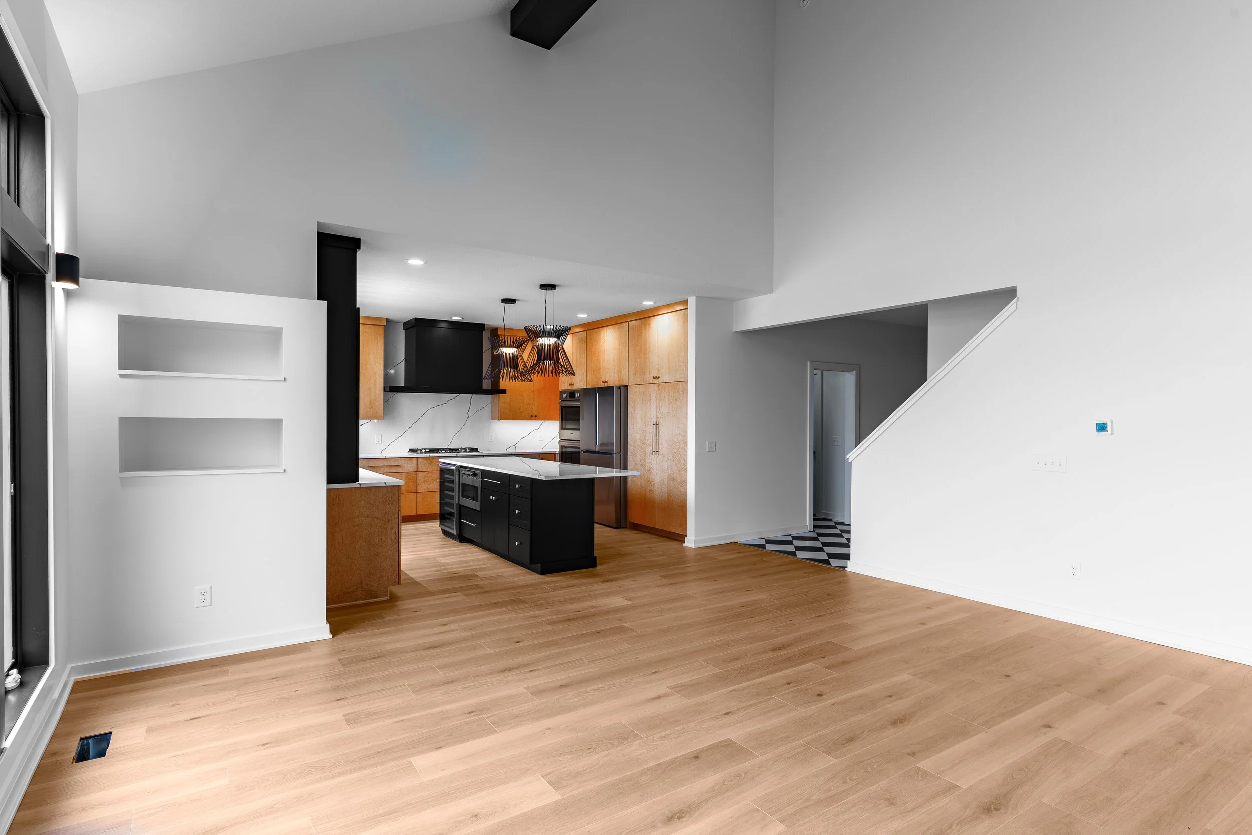 Open-concept living space with hardwood floors, white walls, and a modern kitchen with wooden cabinets, a black island, and pendant lights.