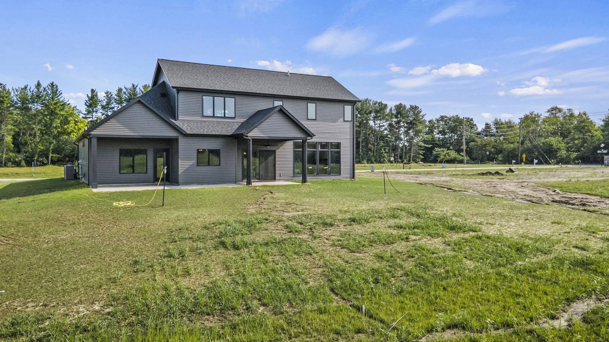 New two-story house with dark gray siding, large windows, and a grassy yard under a blue sky with some clouds.
