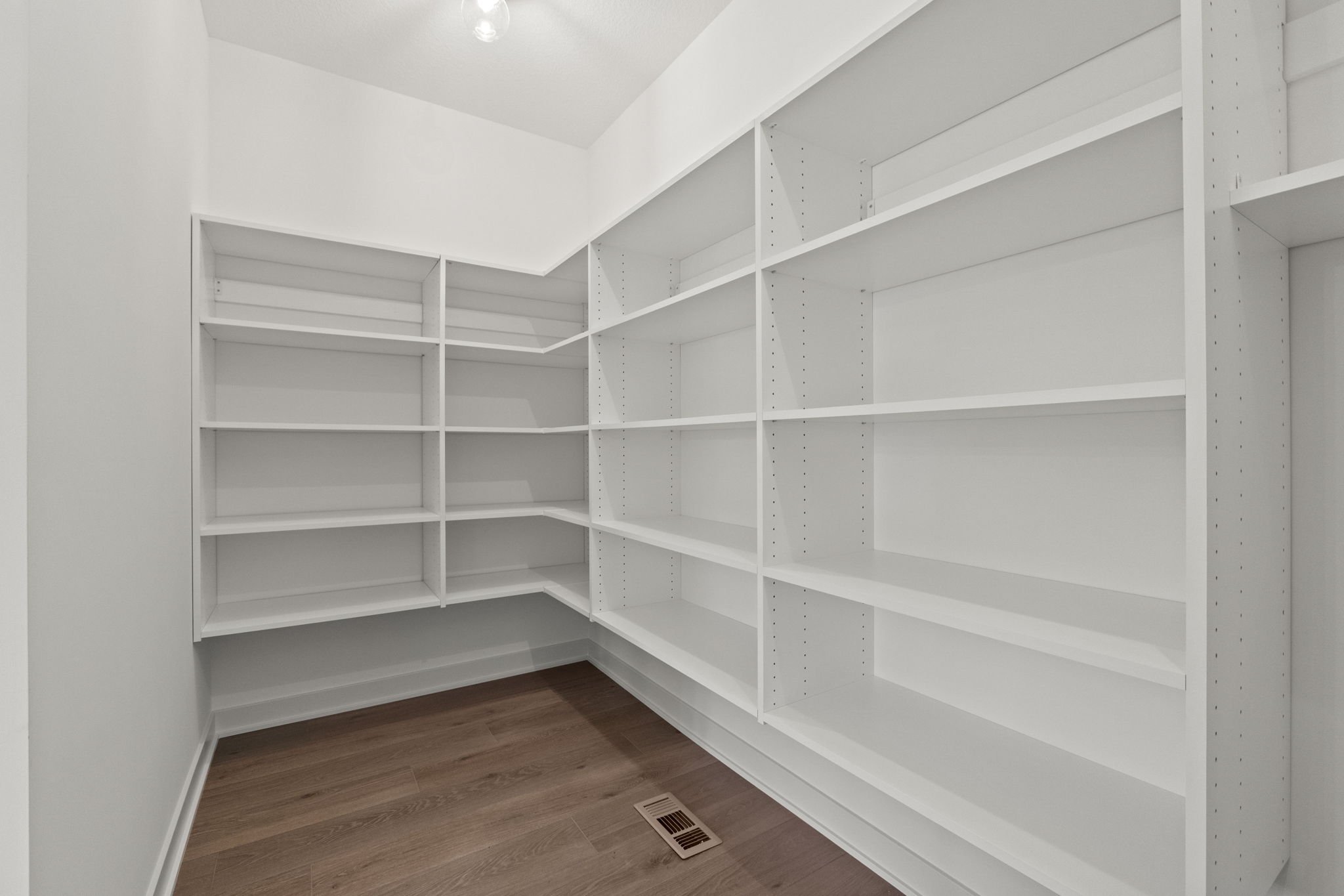 Empty white built-in bookshelf in a corner room with wooden flooring and a ceiling vent.