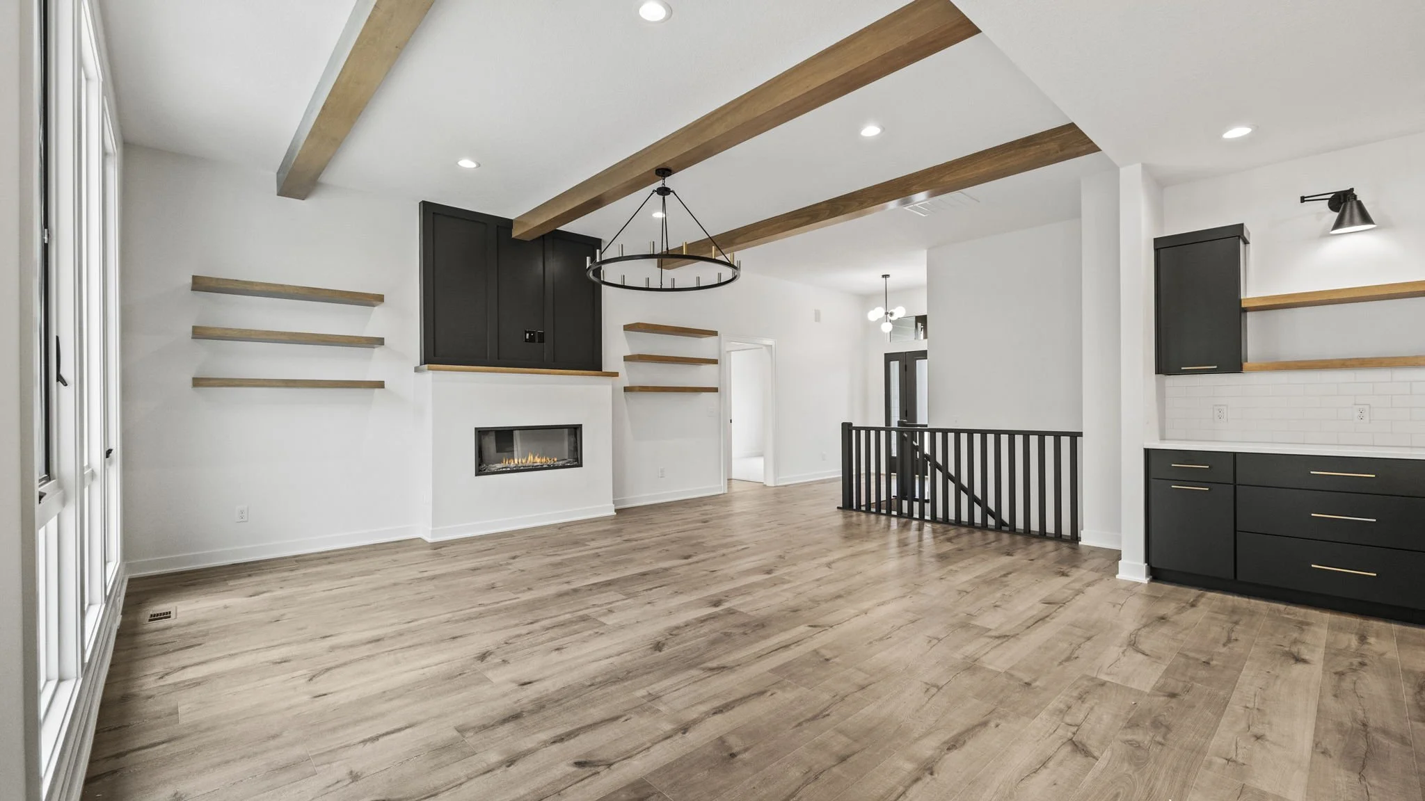 Empty living room with light wood flooring, white walls, black cabinets, a fireplace, open shelves, and a staircase with black railing.