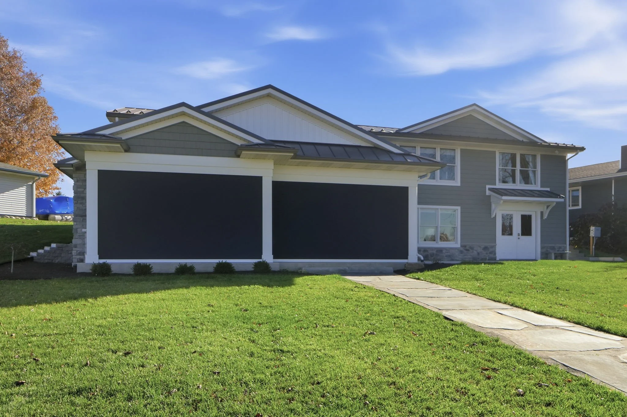 Rear view of a modern two-story house with a grass lawn and a walkway; the house has light gray siding, white trims, a small porch over the front door, and a two-car garage with black doors.