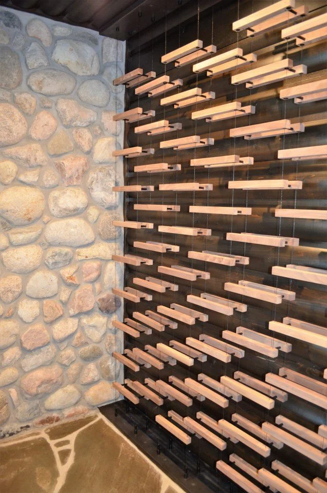 An art installation featuring multiple horizontal wooden planks suspended on thin wires against a dark wooden wall