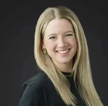 A young woman with long blonde hair smiling against a black background.