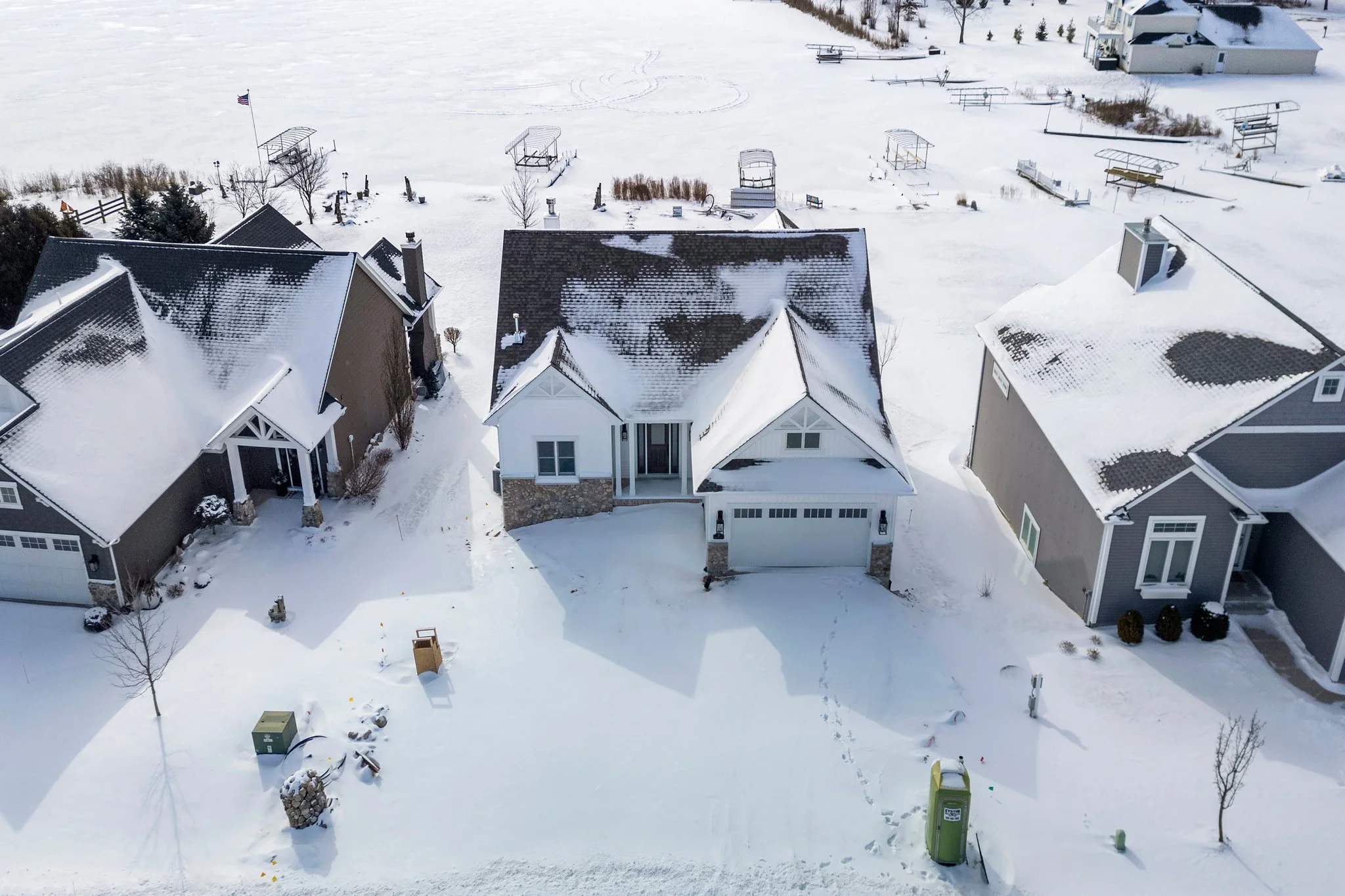 Aerial view of three houses in a snow-covered neighborhood, with footprints in the snow and leafless trees.