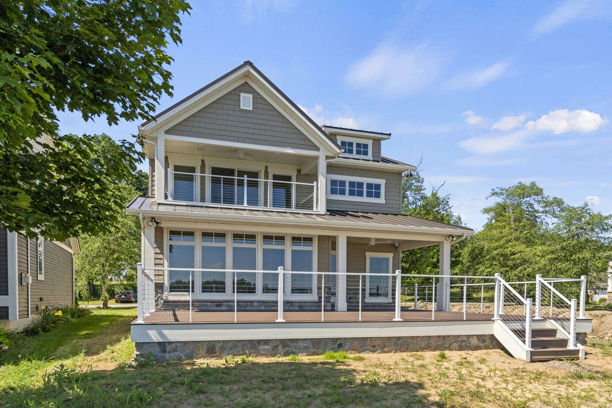 A modern two-story house with large windows, a spacious deck, and a balcony, located in a green suburban area on a clear day.